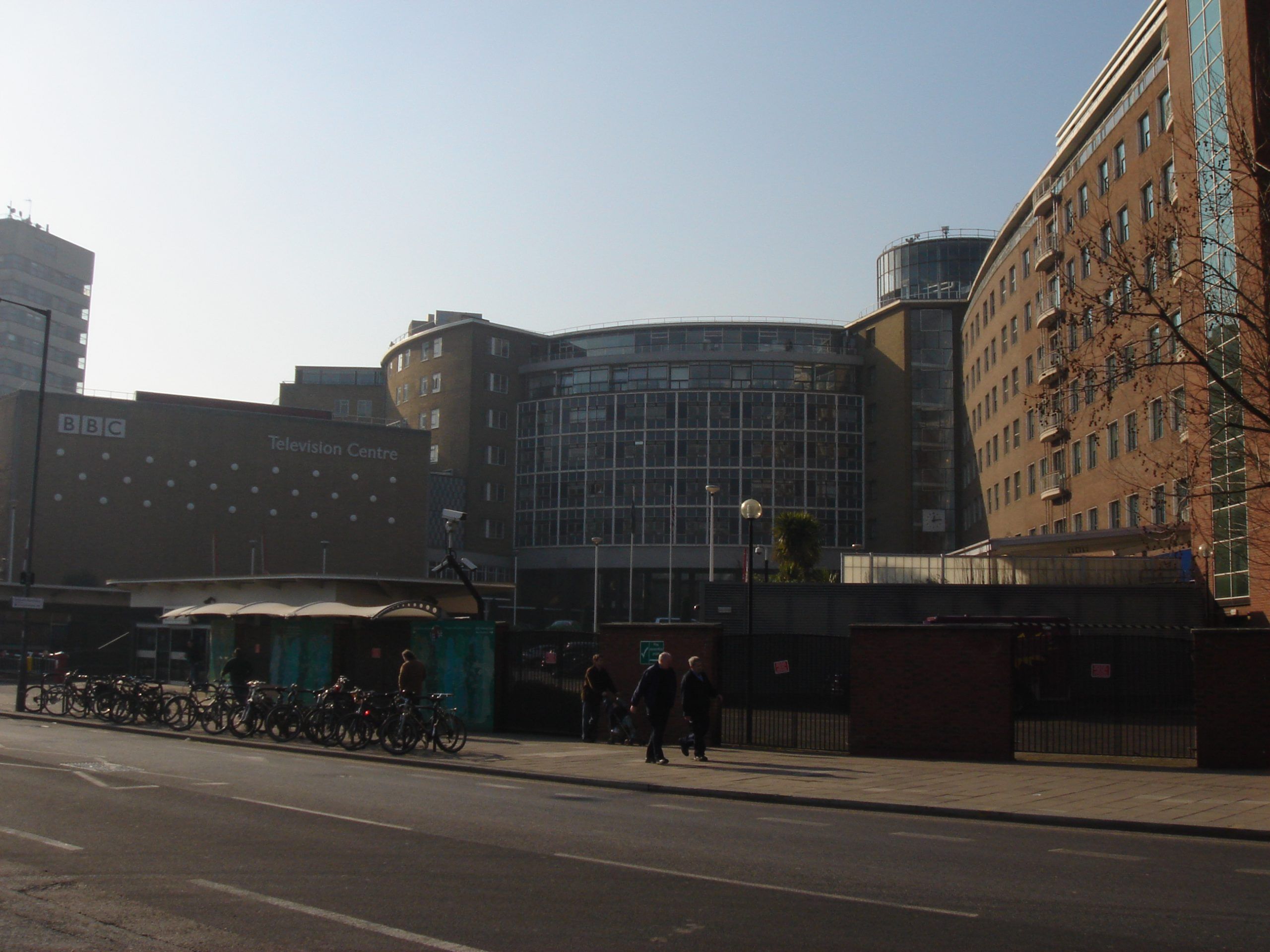 Front entrance of the BBC Television Centre in London, with a security gate, BBC signage, and a curved building in the background.