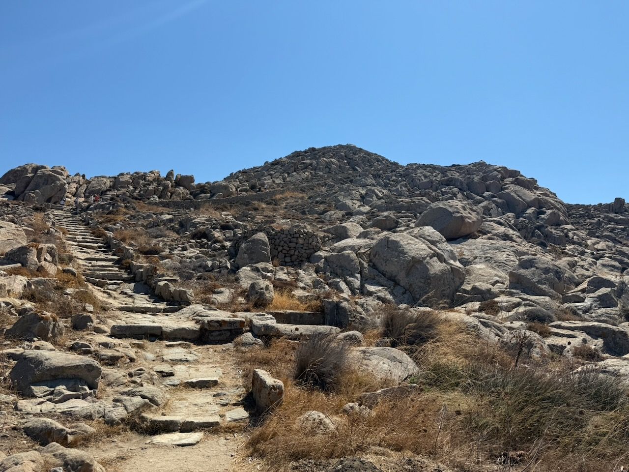 Stones steps lead up to Mount Cynthus, which is low and rocky against the blue sky.