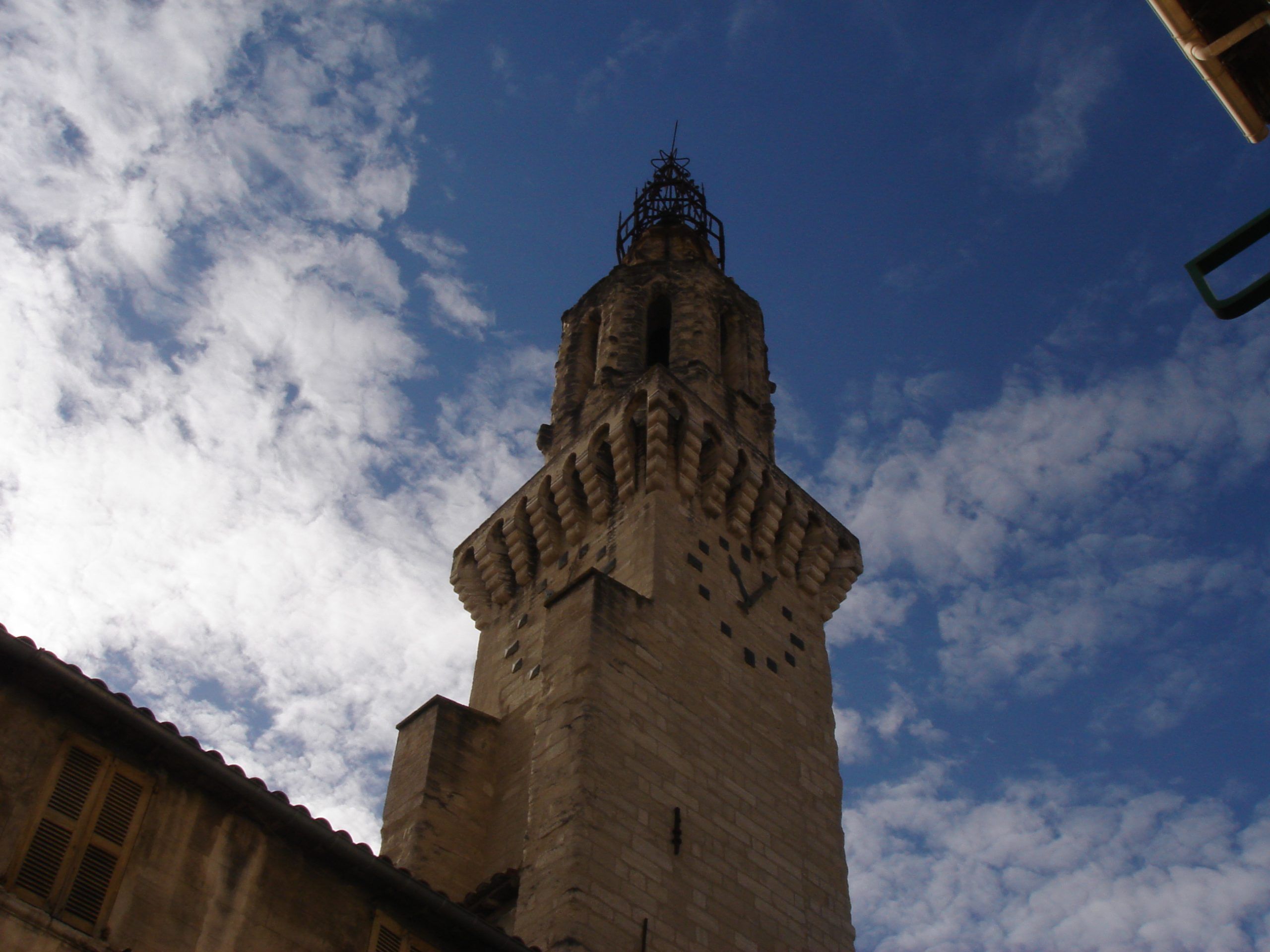 A stone clock tower in Avignon, viewed from below against a partly cloudy sky.