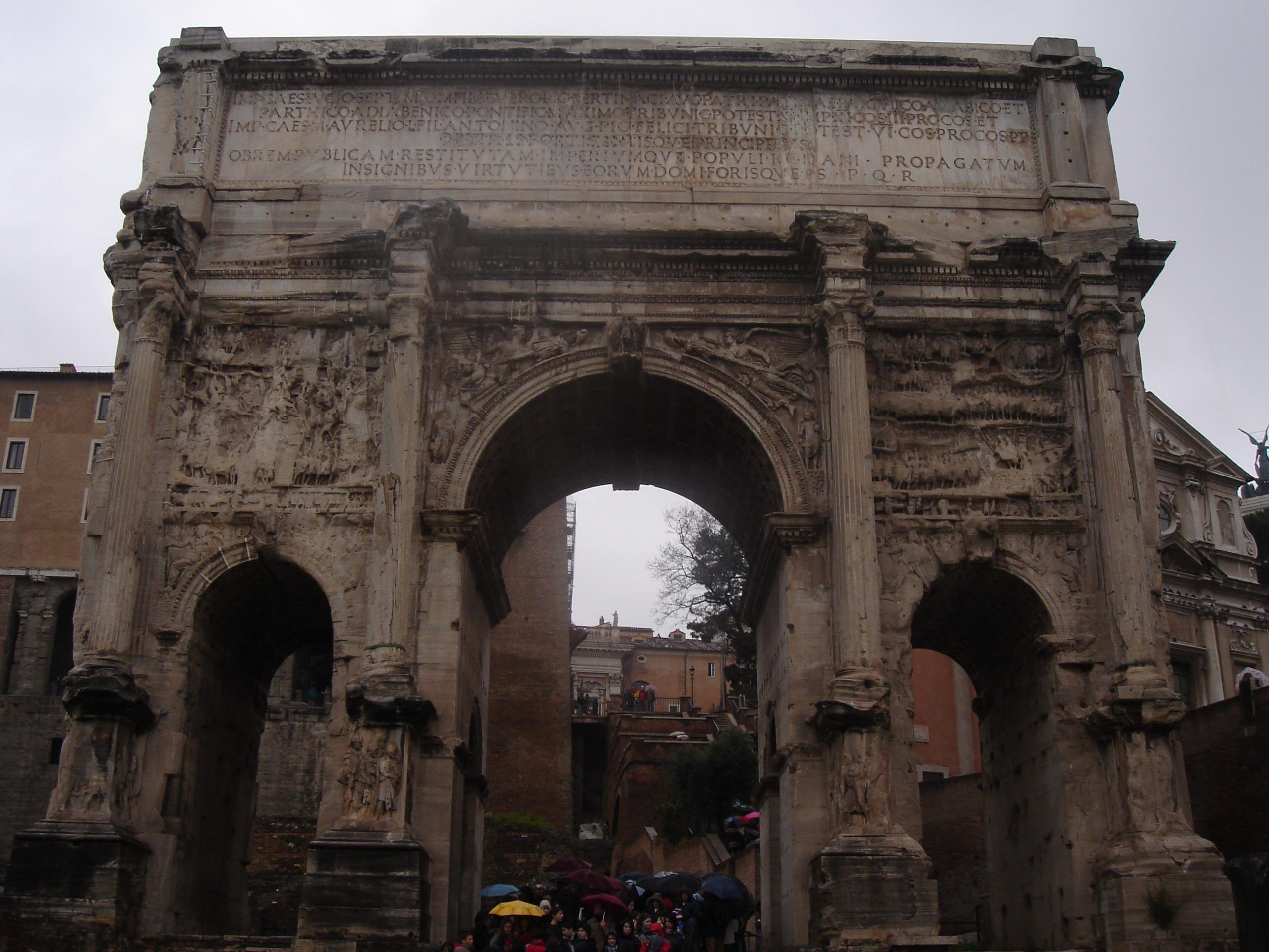 The Arch of Septimius Severus in the Roman Forum, with three arches, detailed relief carvings, and a large Latin inscription above.