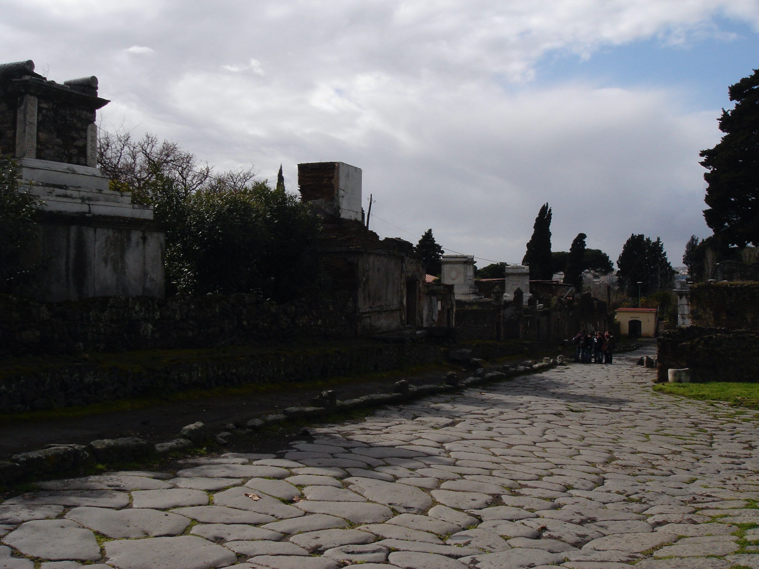 View along a street in Pompeii past worn basalt paving stones and towering tombs near the Nucerian Gate.