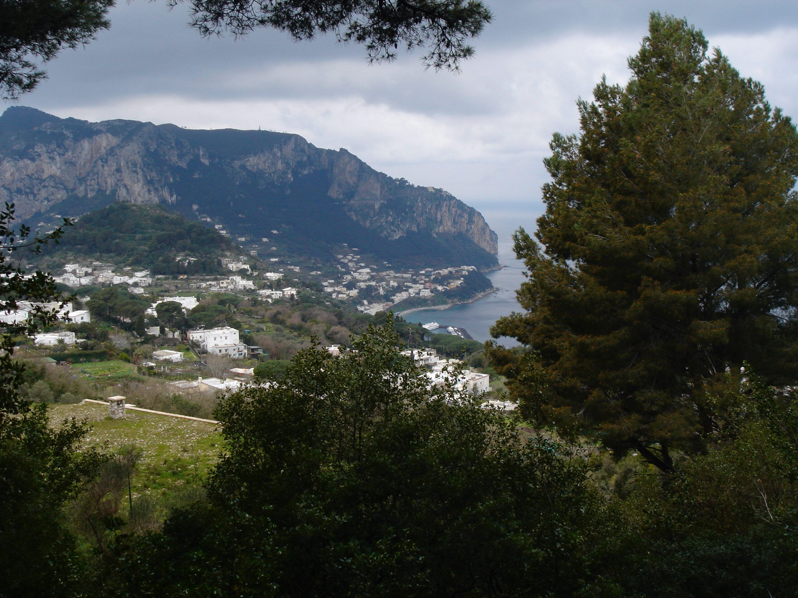 Distant view of whitewashed houses dotting the lush landscape of a mountainous island with cliffs descending to the sea.