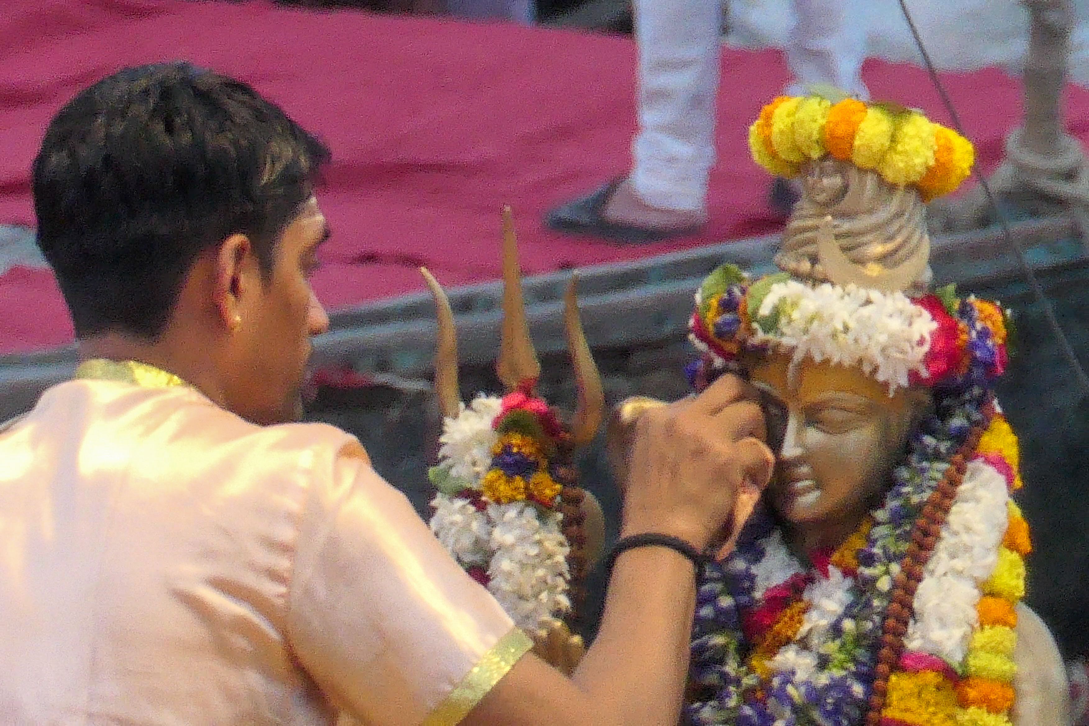 Priest places a tilak on a flower-garlanded statue of Lord Shiva during preparations for Ganga Aarti.