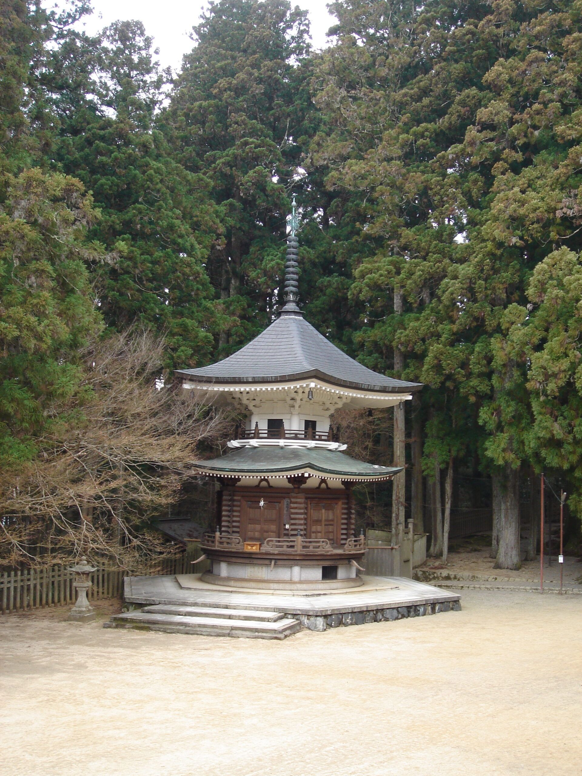 A small wooden pagoda-style temple surrounded by tall forest trees.