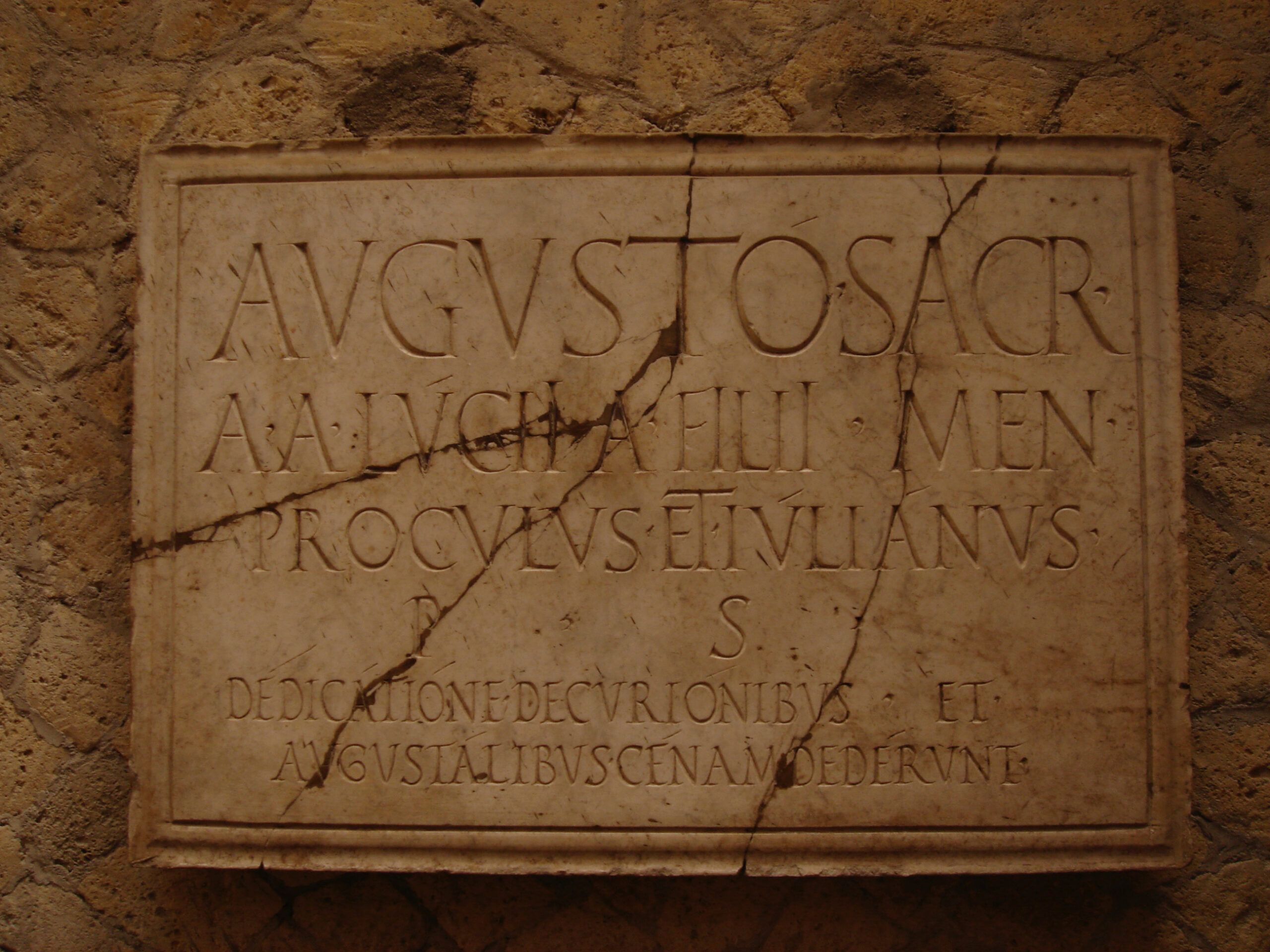 Stone plaque inscribed in Latin dedicating a structure to Augustus, mounted on the wall of a Roman building in Herculaneum.