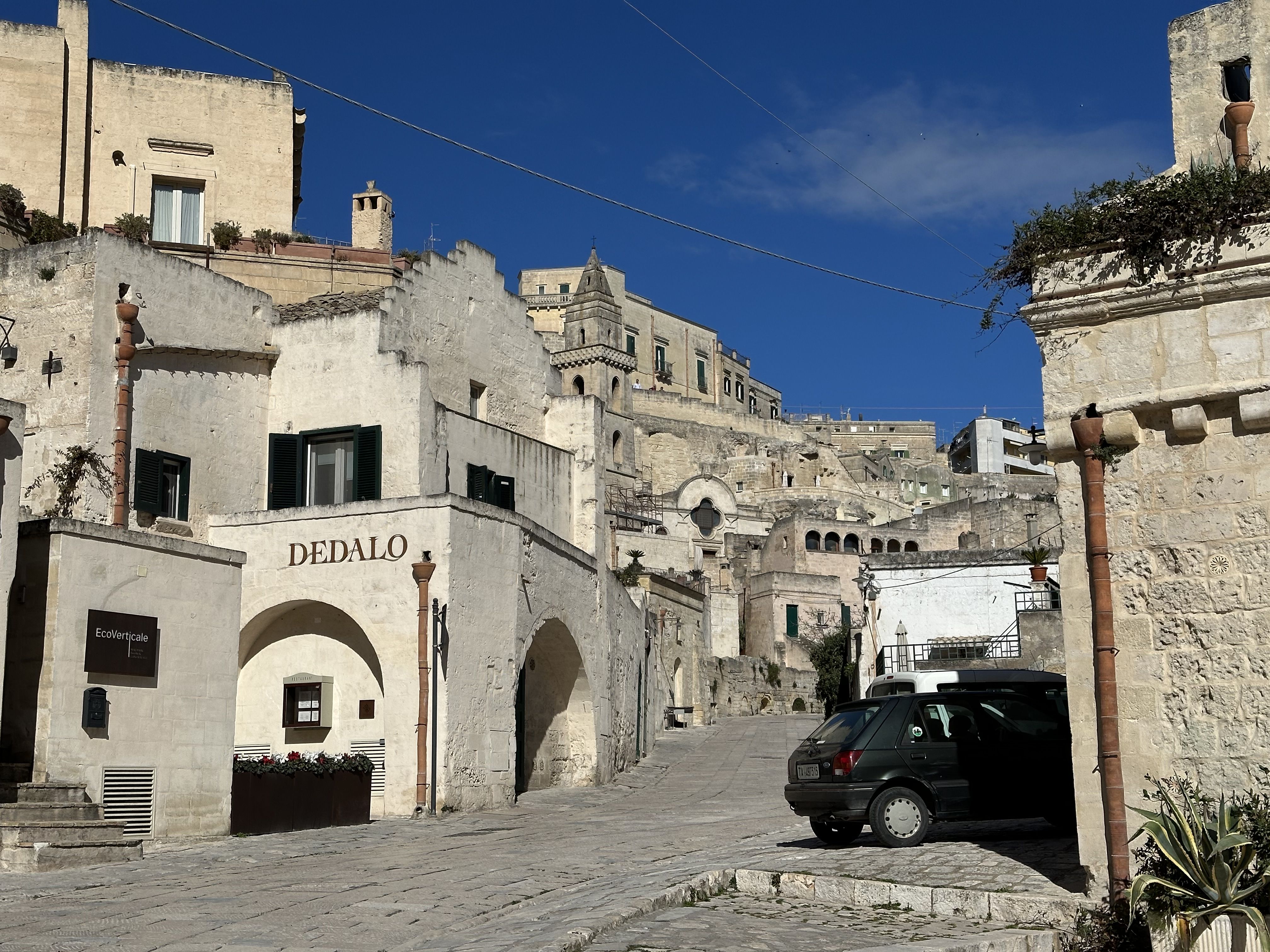 Steep cobbled street in Matera lined with pale stone buildings, including a restaurant named “Dedalo”.