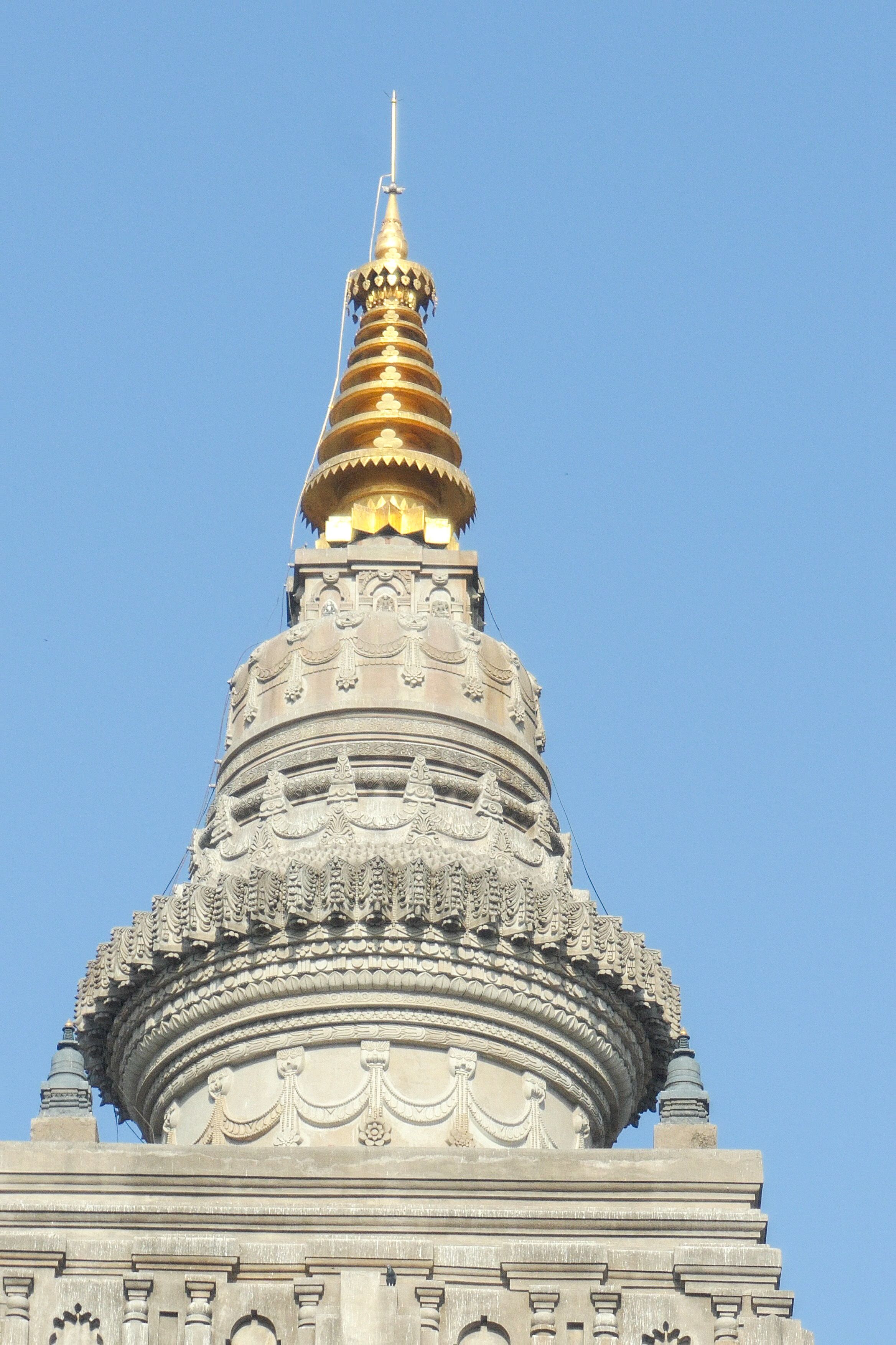 Close-up of the intricately carved golden spire atop the Mahabodhi Temple against a bright blue sky.