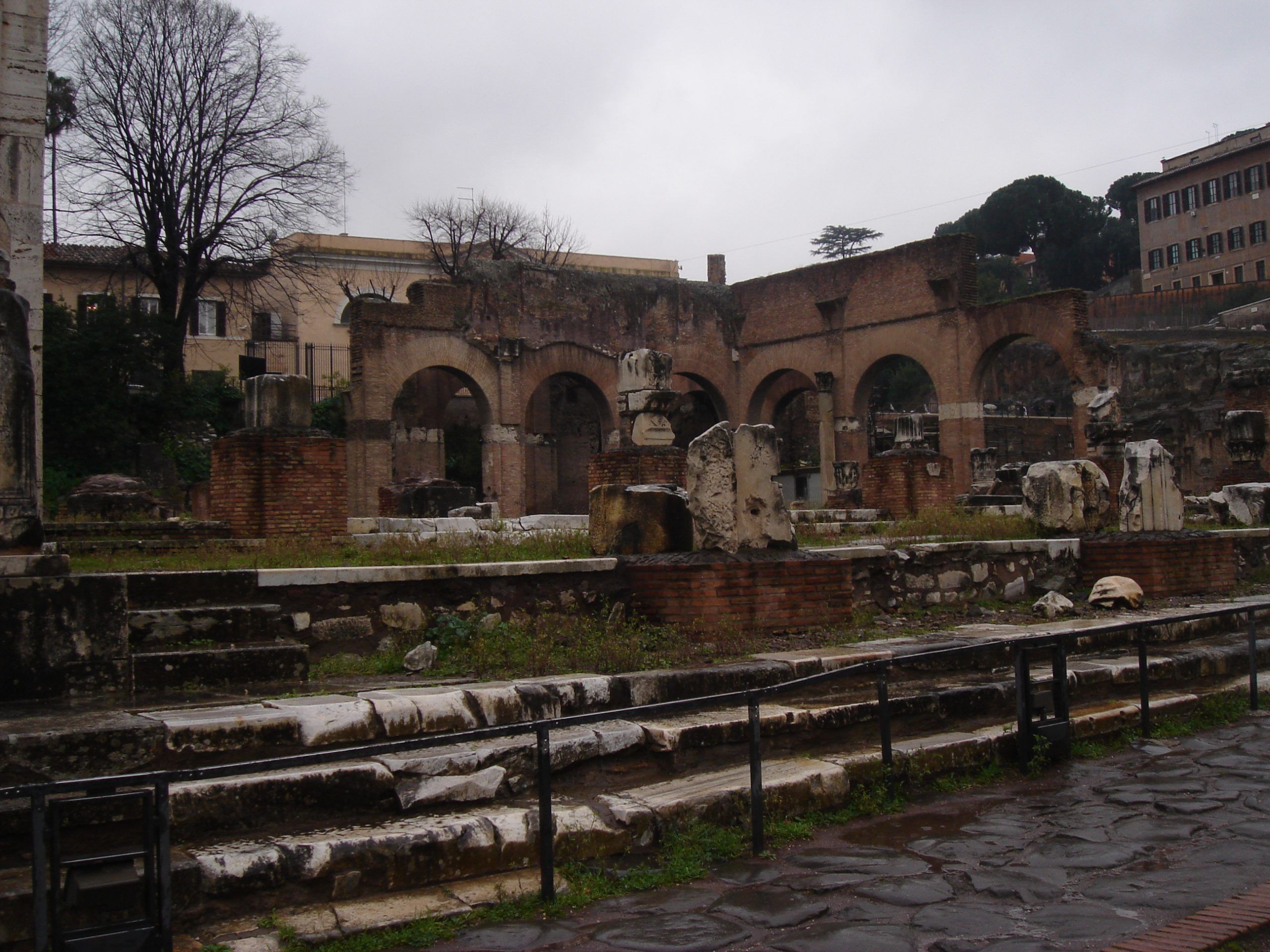 Ruins of the Basilica Aemilia in the Roman Forum, with broken columns, scattered marble fragments, and brick arches in the background.