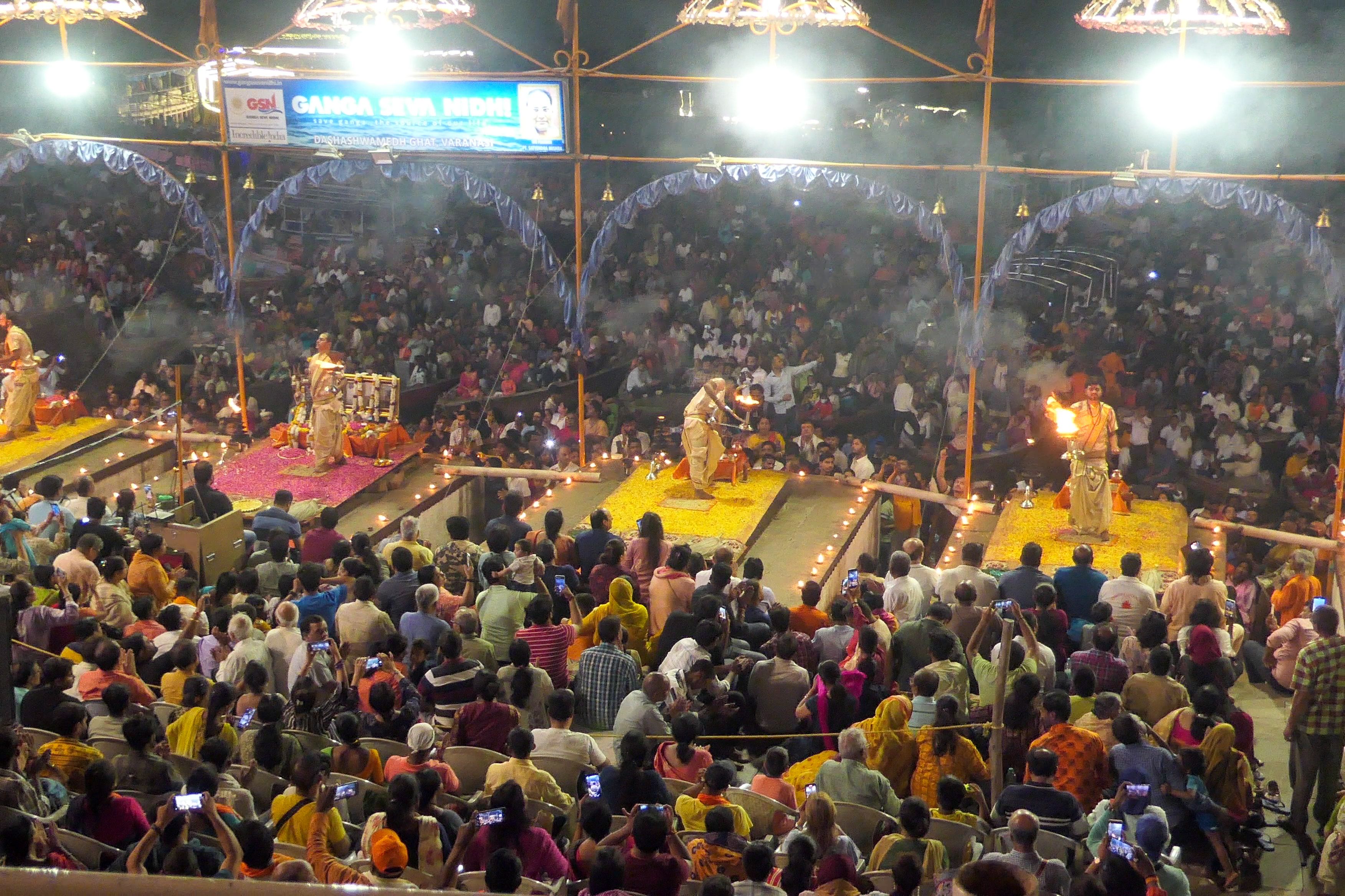 Large crowd gathers at Dashashwamedh Ghat in Varanasi for the evening Ganga Aarti, with priests performing rituals with fire on raised platforms.