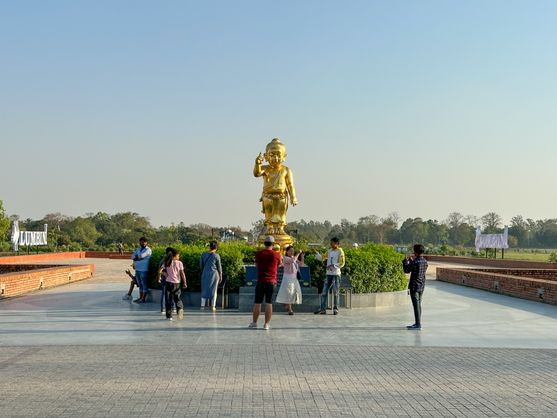 A two-metre statue of the baby Buddha pointing up at the sky. It's on a plinth surrounded by people.