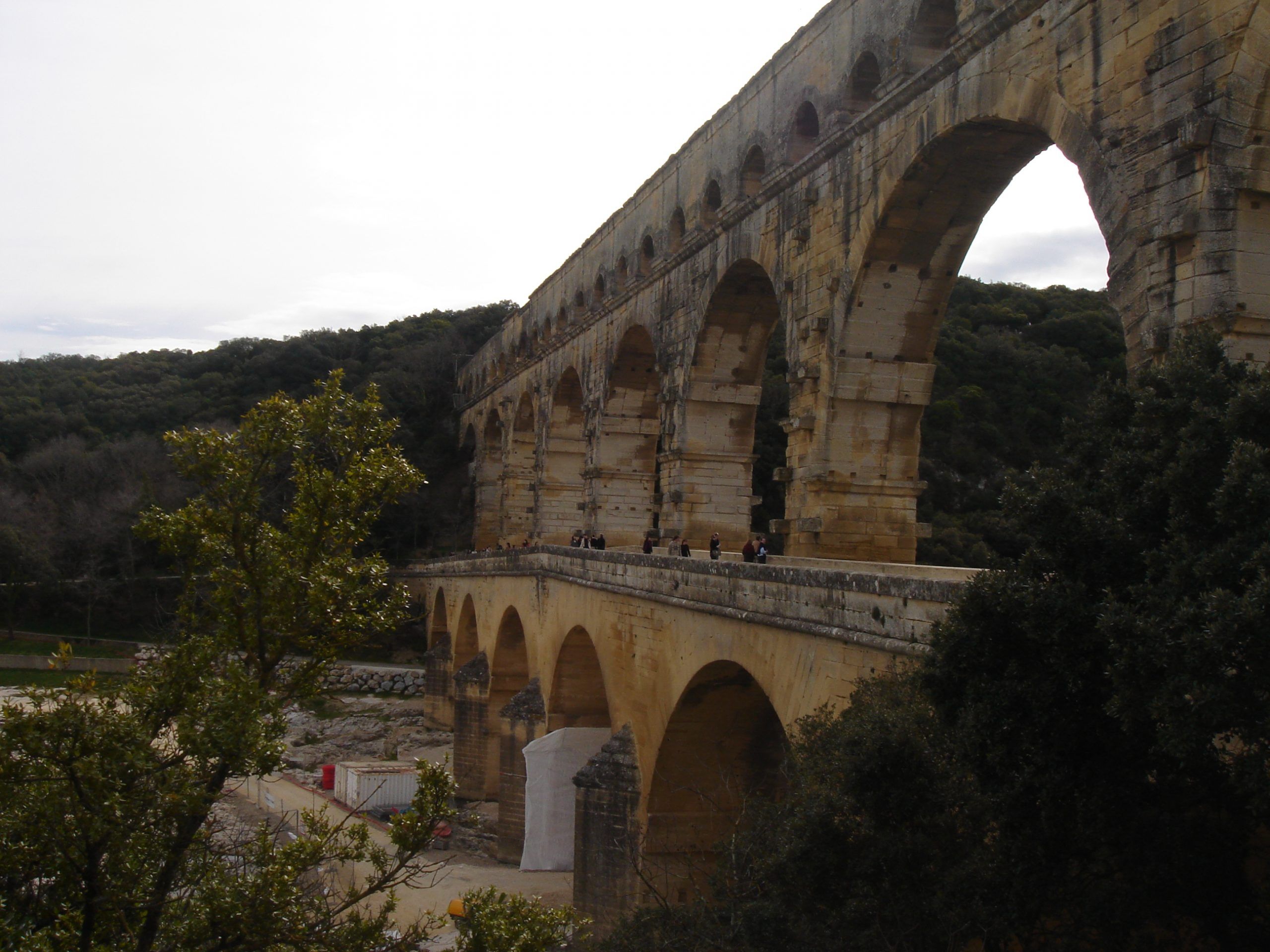 Angled view of the Pont du Gard showing its three tiers of arches spanning the river, with visitors walking along the lower level.