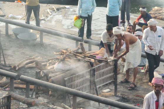 A traditional Hindu cremation ceremony taking place at a riverside ghat in Varanasi, with family members tending to the funeral pyre amid rising smoke.