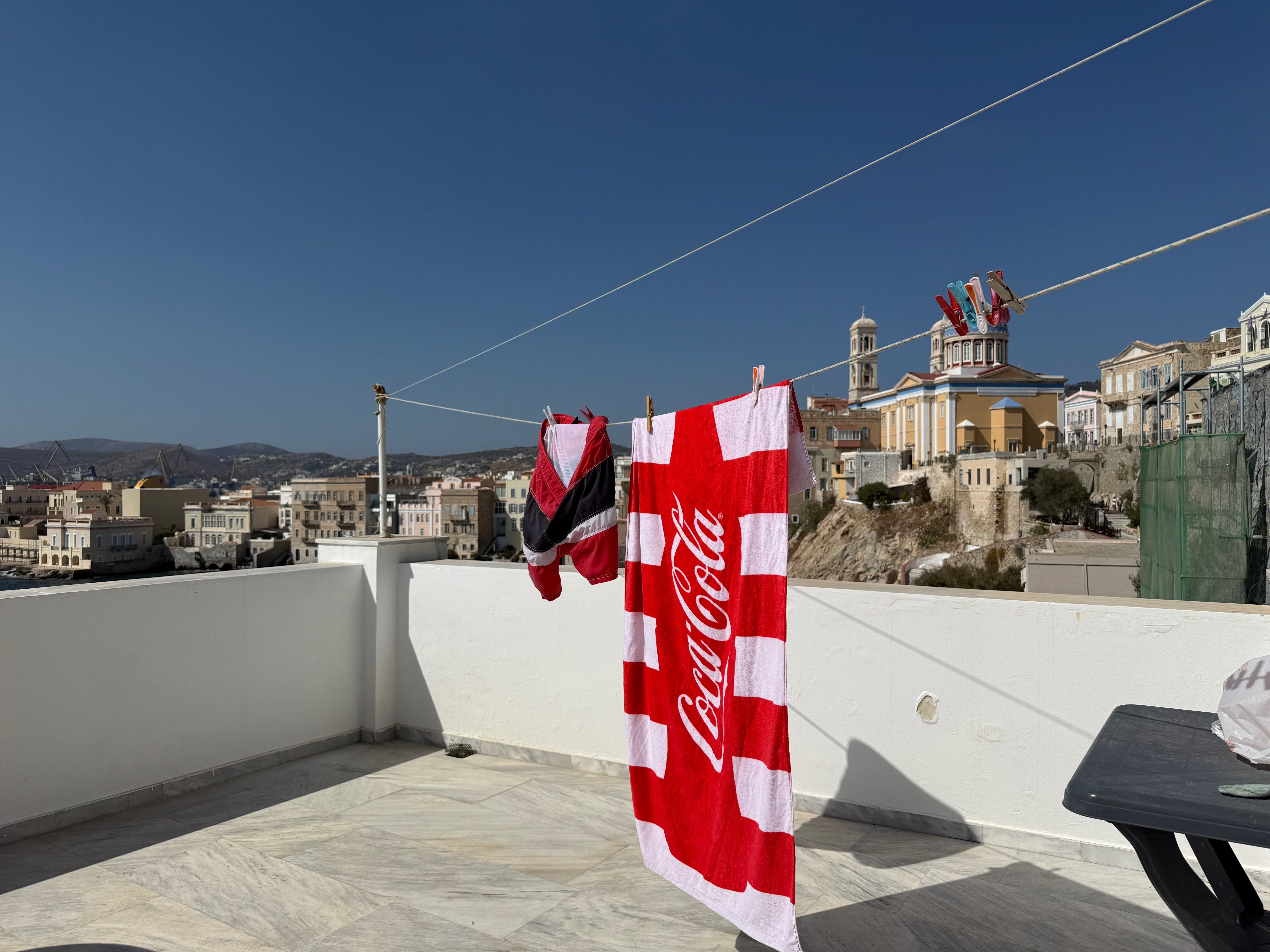 The terrace overlooking the beach. Swimming shorts and a Coke branded beach towel are drying on a line. The sky is clear and sunny.