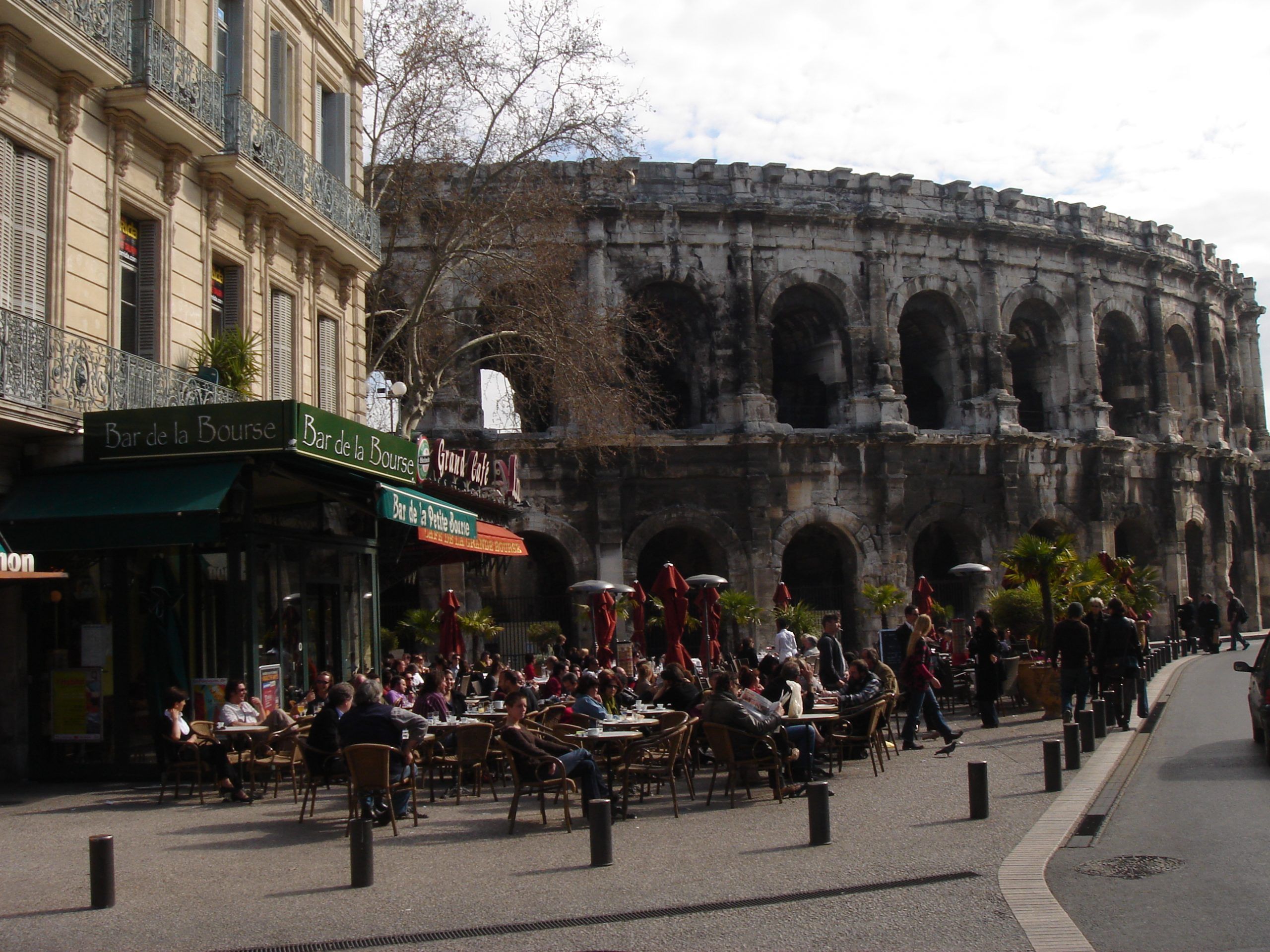 Busy café scene in Nîmes with diners sitting outside near the Roman amphitheatre.