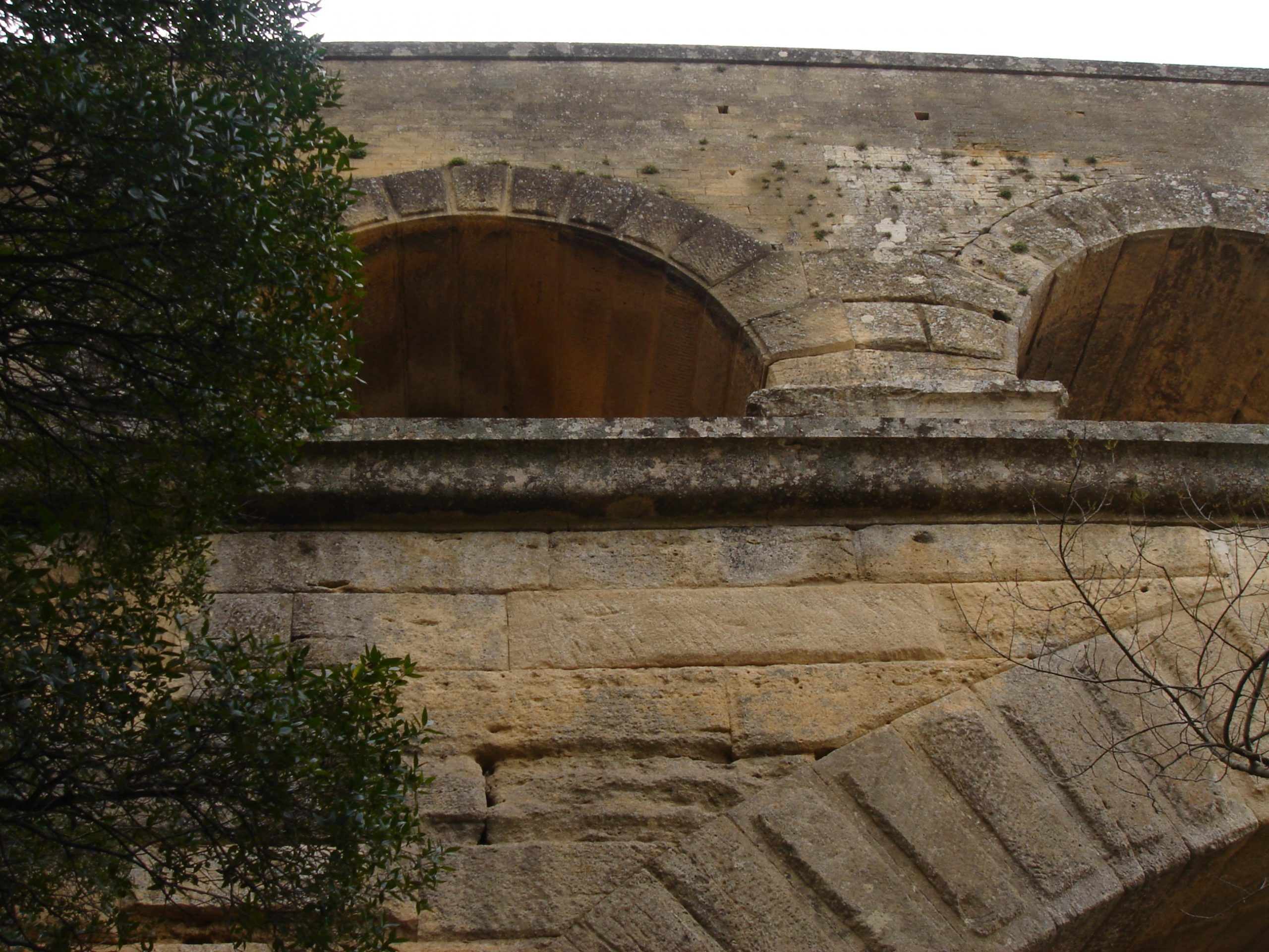 Close-up view of the mid-tier arches of the Pont du Gard, seen from below with stone details partially obscured by trees.