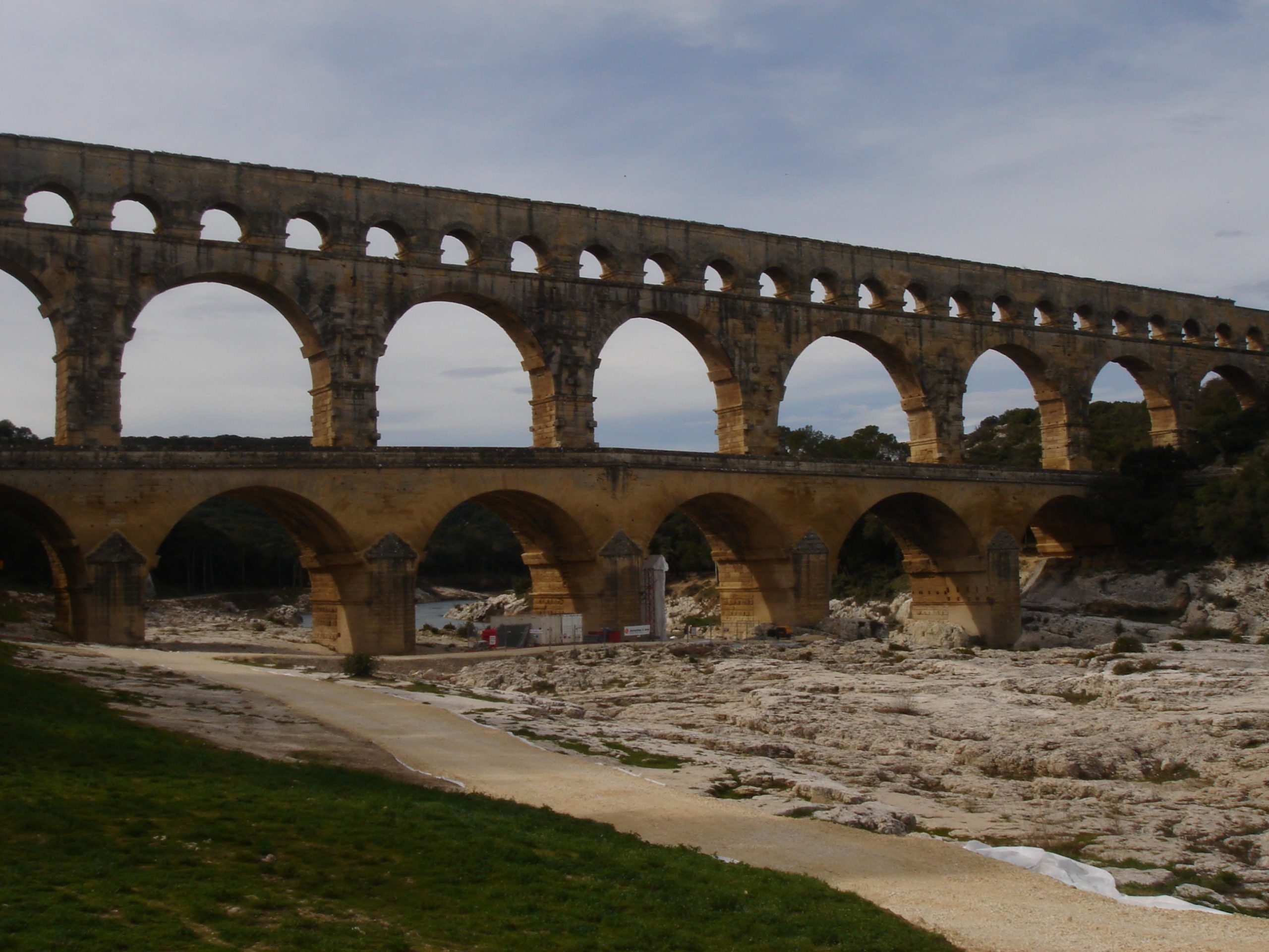 Side view of the full span of the Pont du Gard aqueduct crossing a rocky riverbed, with a clear view of all three tiers of arches.