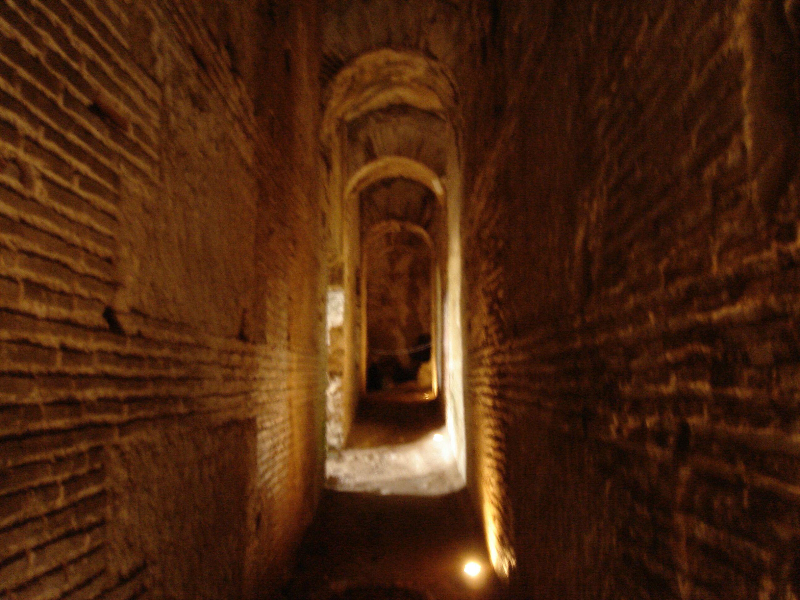 Dimly lit, ancient brick corridor with rounded archways, leading into the archaeological ruins of Villa Jovis.