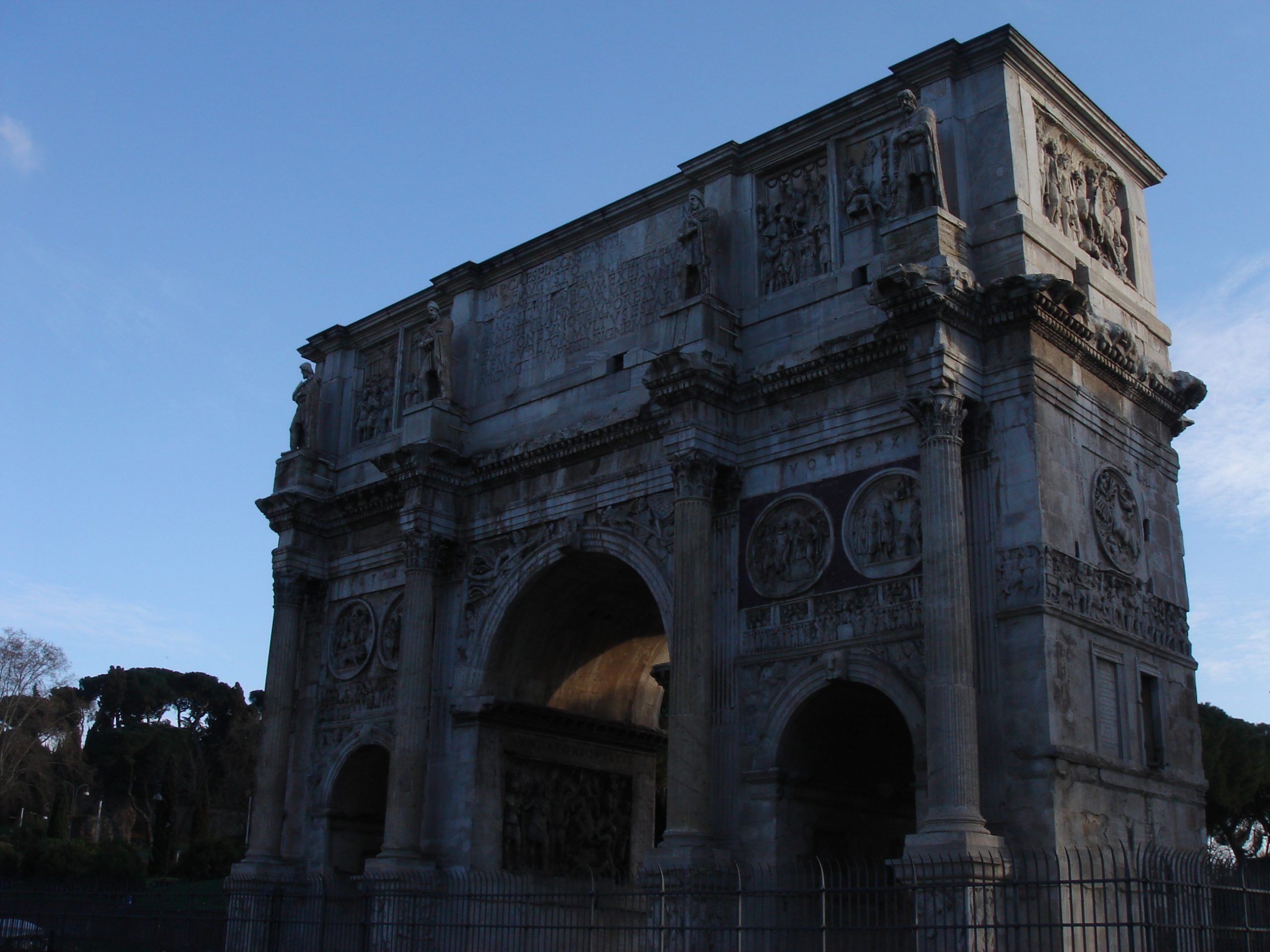The Arch of Constantine near the Colosseum, seen in shadow with intricate reliefs and sculpted figures.
