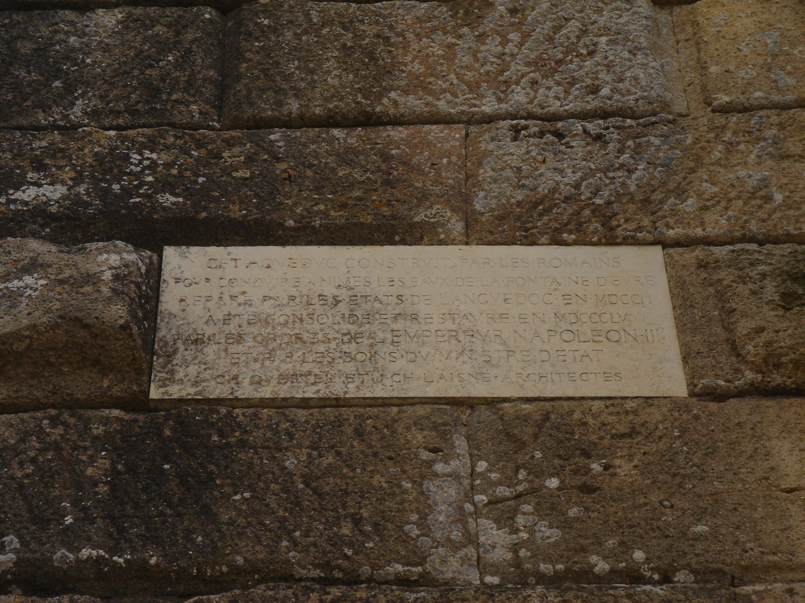 Commemorative stone plaque in French embedded in the Pont du Gard, describing its Roman construction and later restoration.