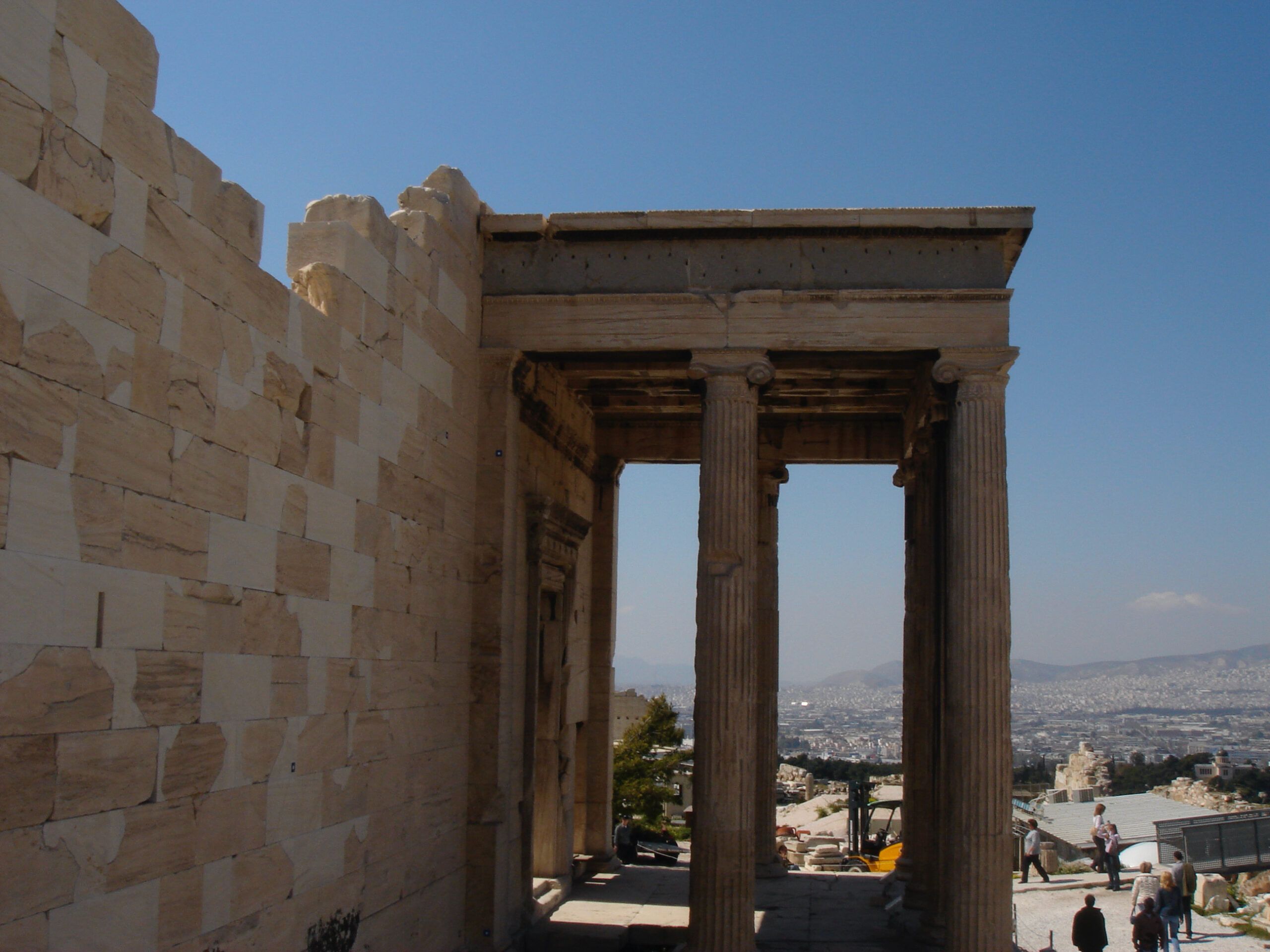 The Erechtheion on the Acropolis with its Caryatid Porch, seen from a distance amid scattered ruins and wildflowers.