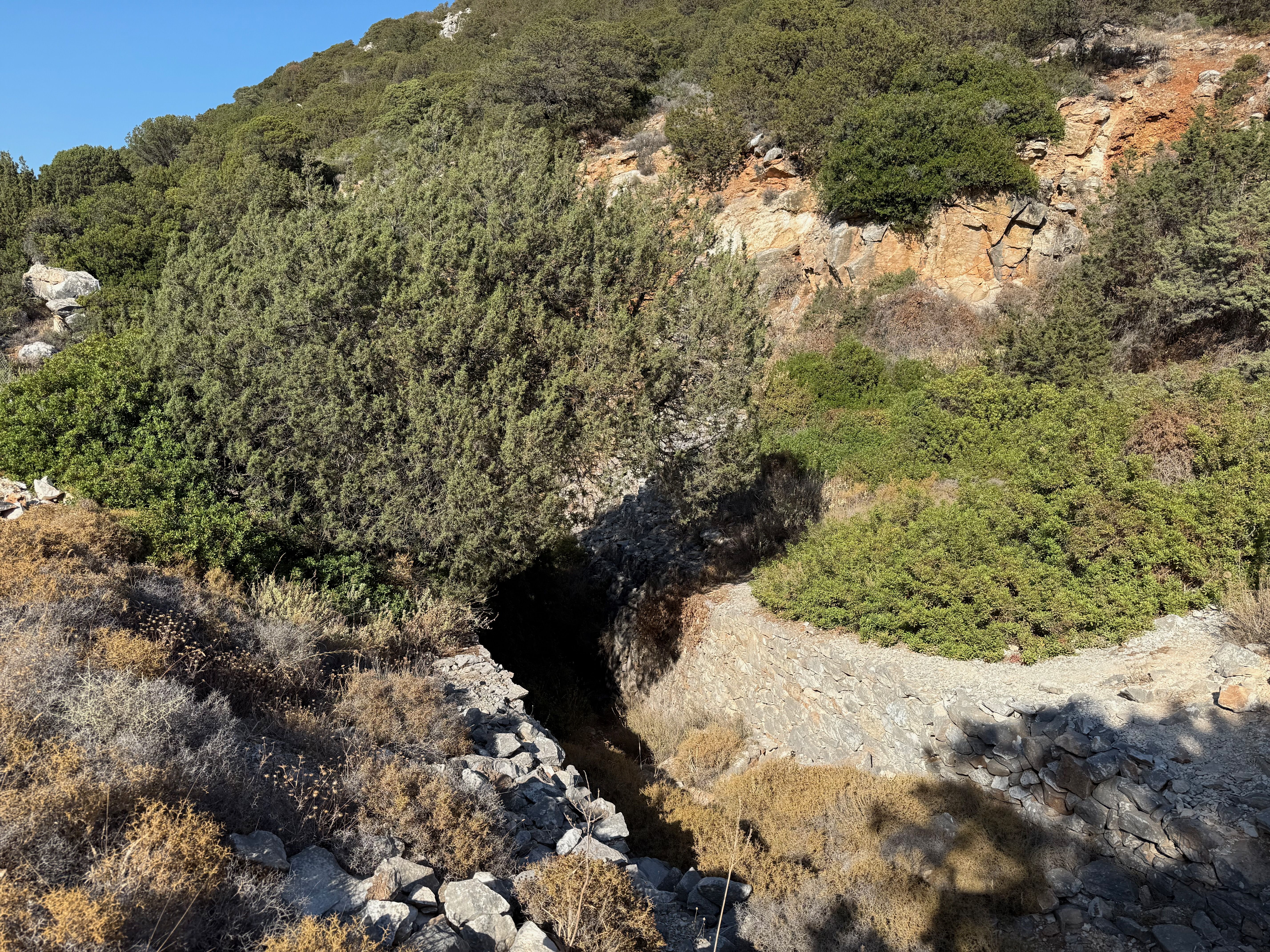 Looking down into the quarry. There's a pathway lined with low walls made of marble stones leading down into a dark hole in the ground.