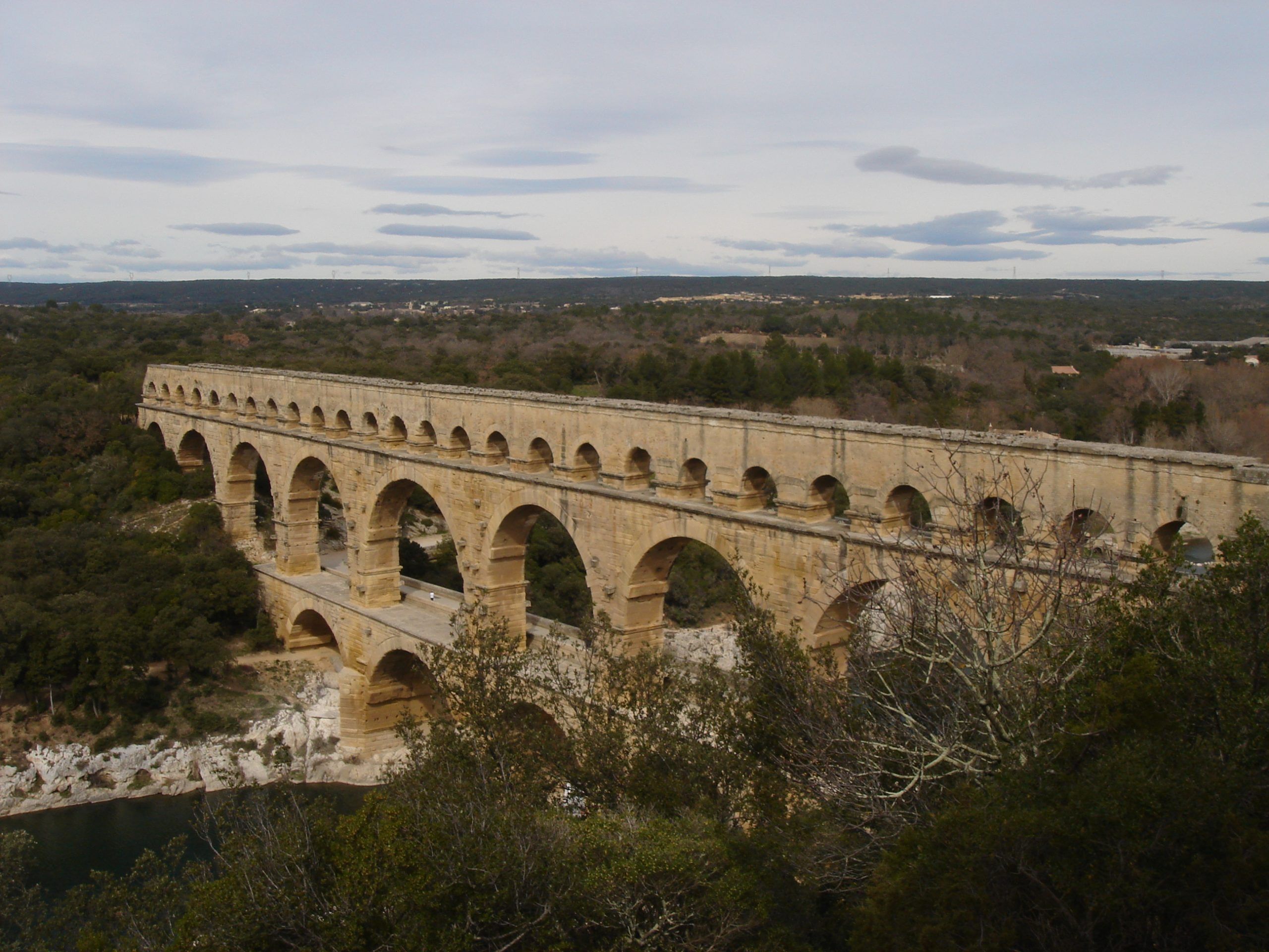 Elevated view of the Pont du Gard aqueduct from a hillside, with the structure stretching across the wooded valley and river below.