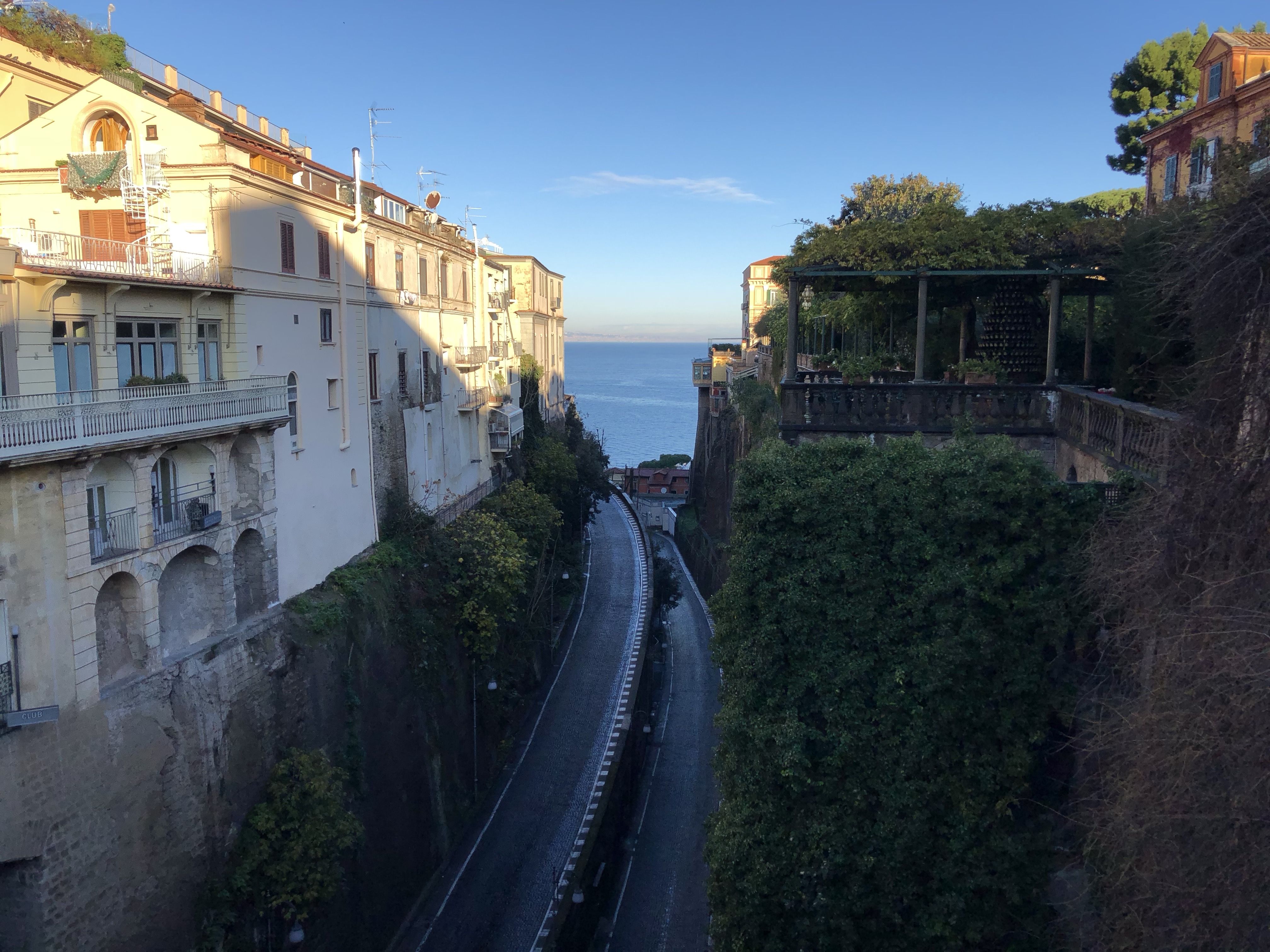 Far below, a road runs through a cutting between two cliffs. There are old buildings perched on each of the cliffs, probably hotels. 