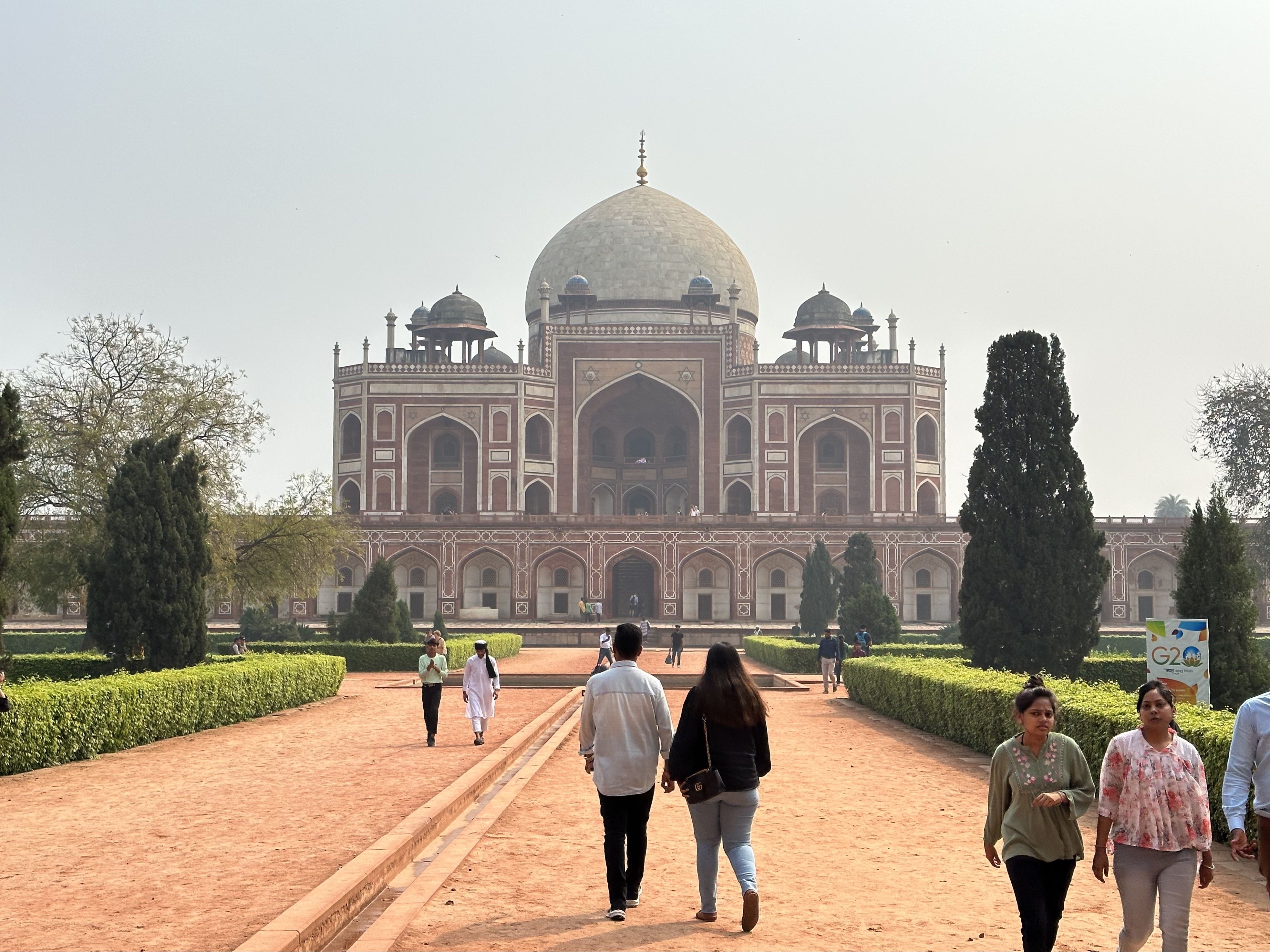 Visitors walking along a red gravel path toward Humayun’s Tomb, a Mughal-era mausoleum with a large dome and arched entrances.