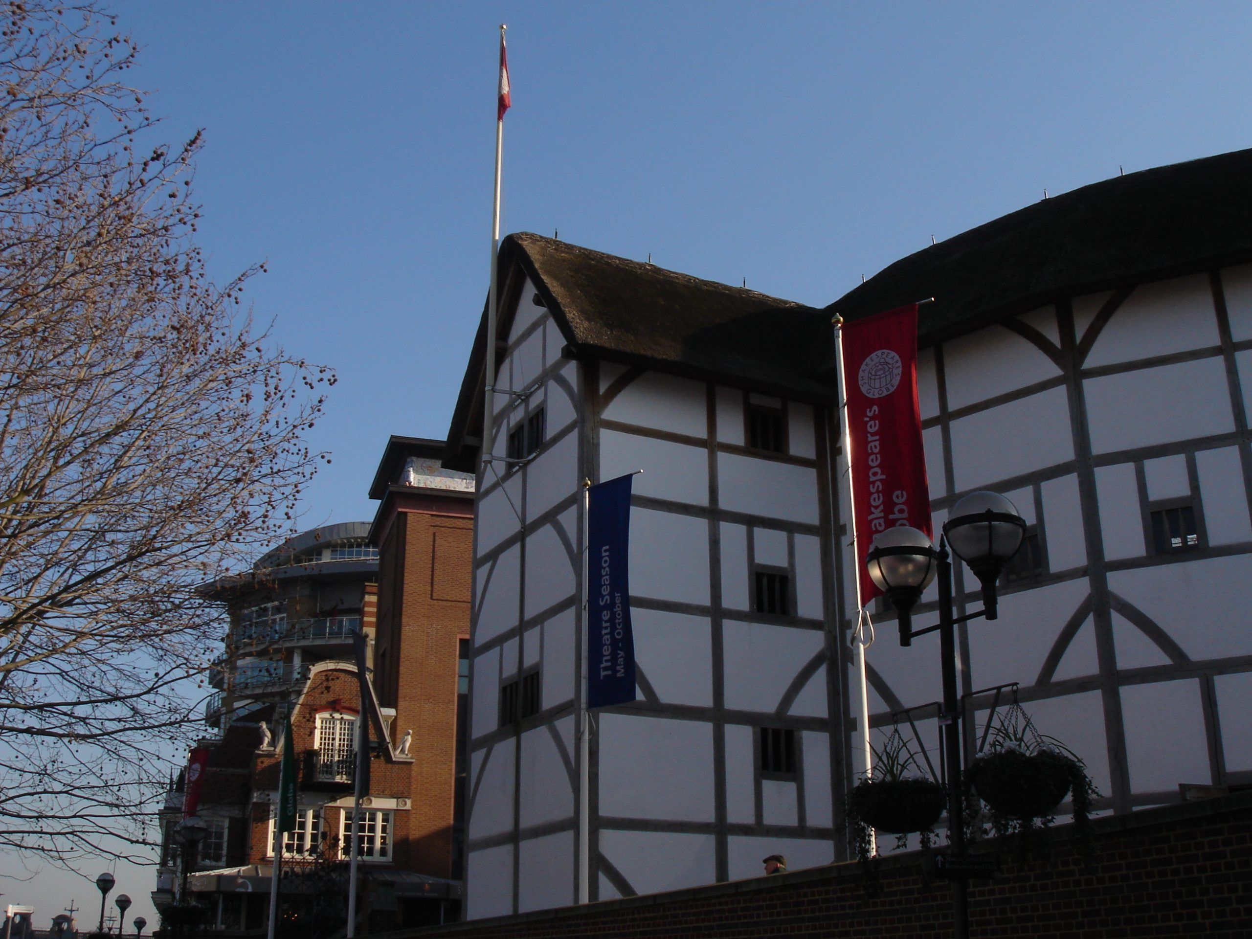 Exterior view of Shakespeare's Globe Theatre in London, showing its half-timbered design, banners, and a lamppost in the foreground.