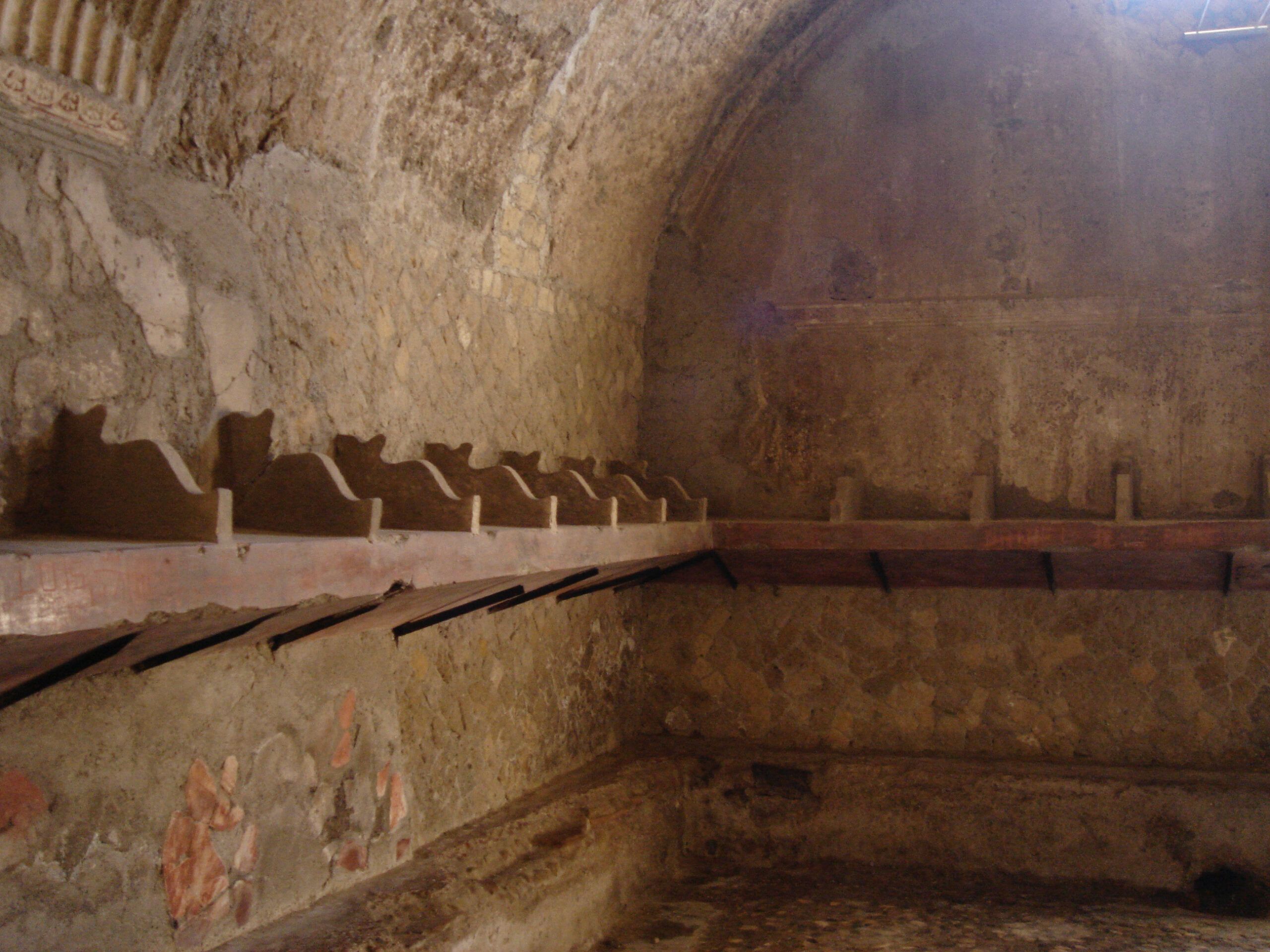 Interior of a Roman bathhouse in Herculaneum, with a vaulted ceiling and a row of cubbyholes or niches along the wall, possibly for storing clothing or belongings.