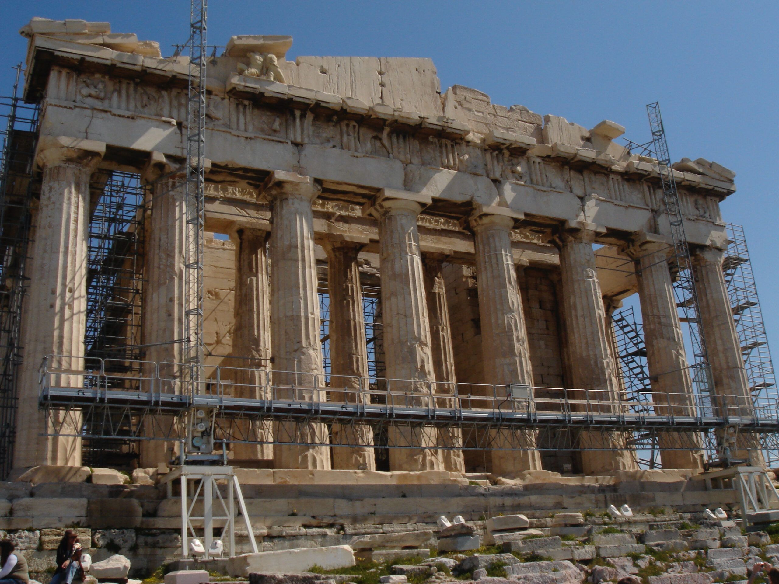 Front view of the Parthenon covered in scaffolding for restoration, with ancient marble columns under a bright sky.