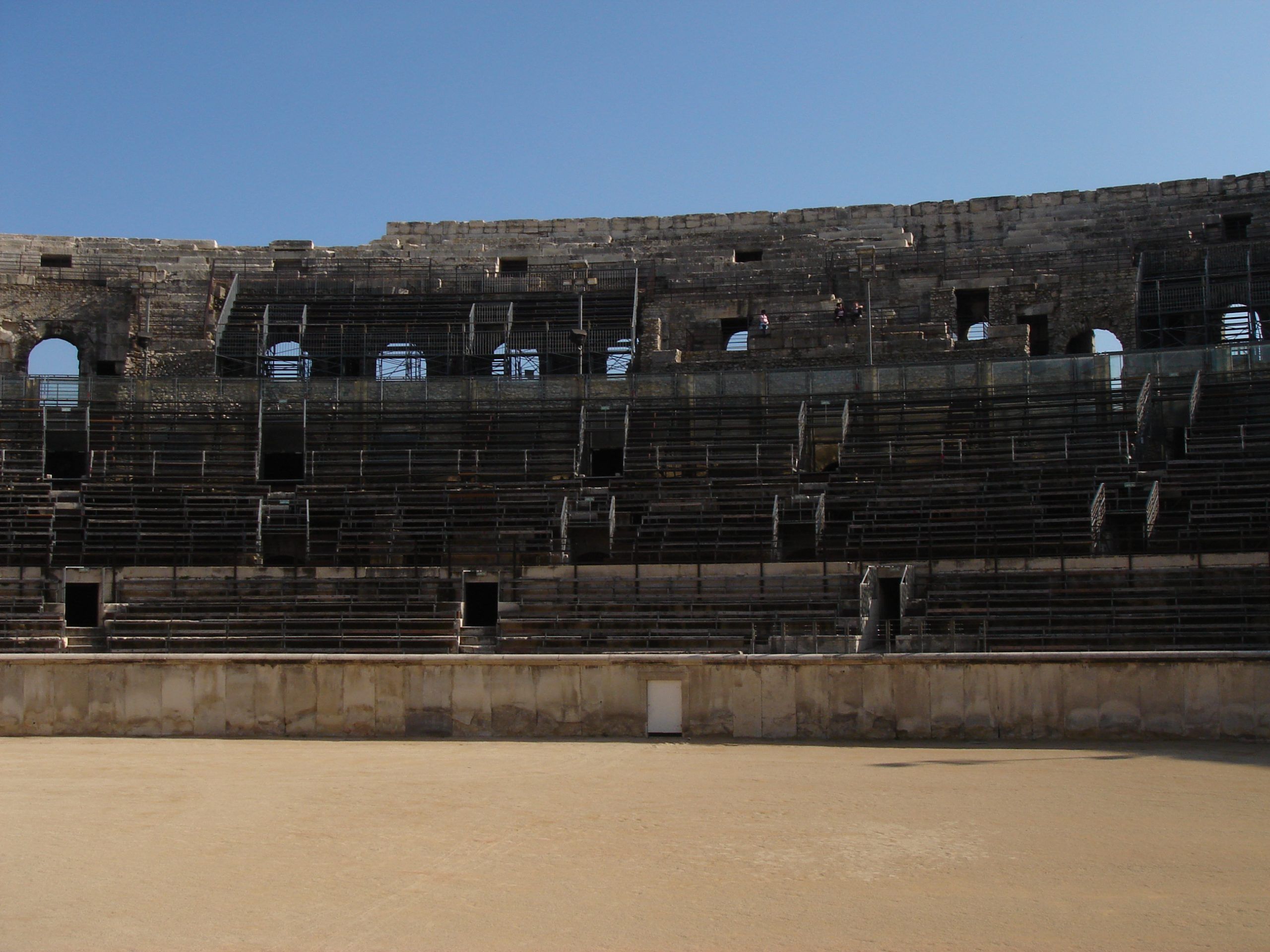 Seating tiers inside the Roman amphitheatre in Nîmes, viewed from the arena floor under a clear blue sky.