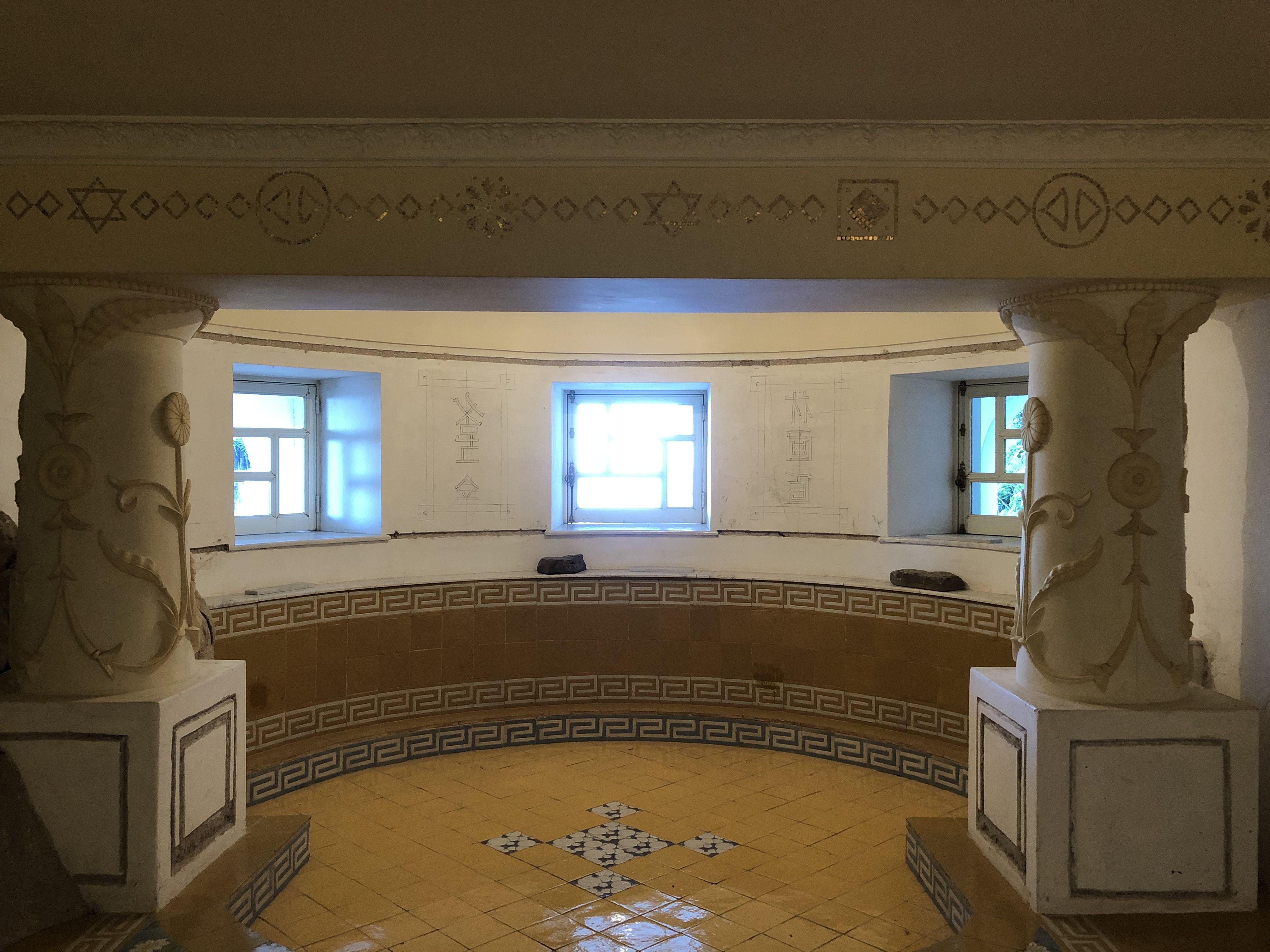Tiled opium room at Villa Lysis with decorated columns, symbolic motifs on the walls, and a semicircular bench under three small windows.