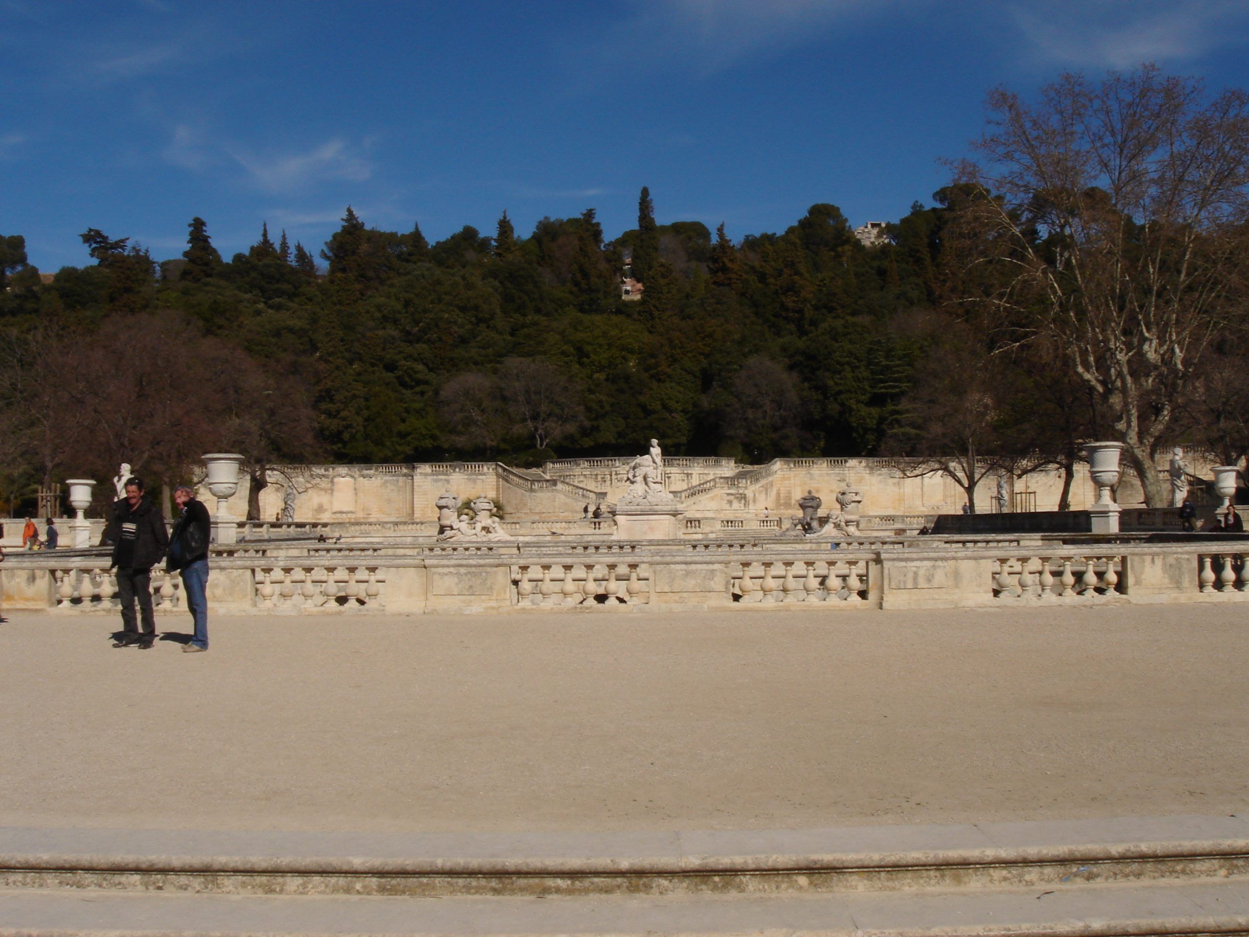 Two men standing in a formal garden in front of the grand staircase and sculptures in the Jardins de la Fontaine.