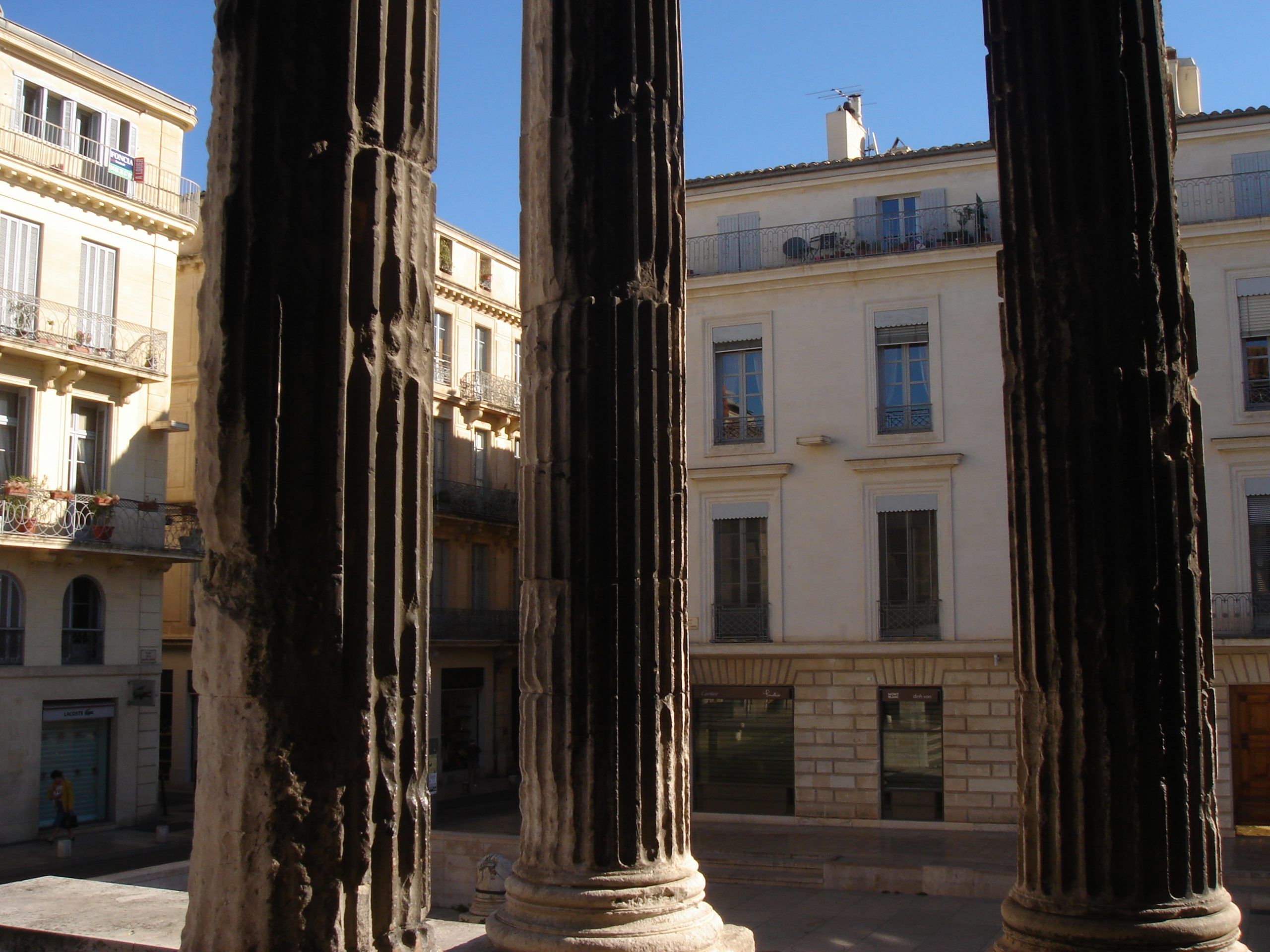 View from behind the columns of the Maison Carrée looking across the street to residential buildings.