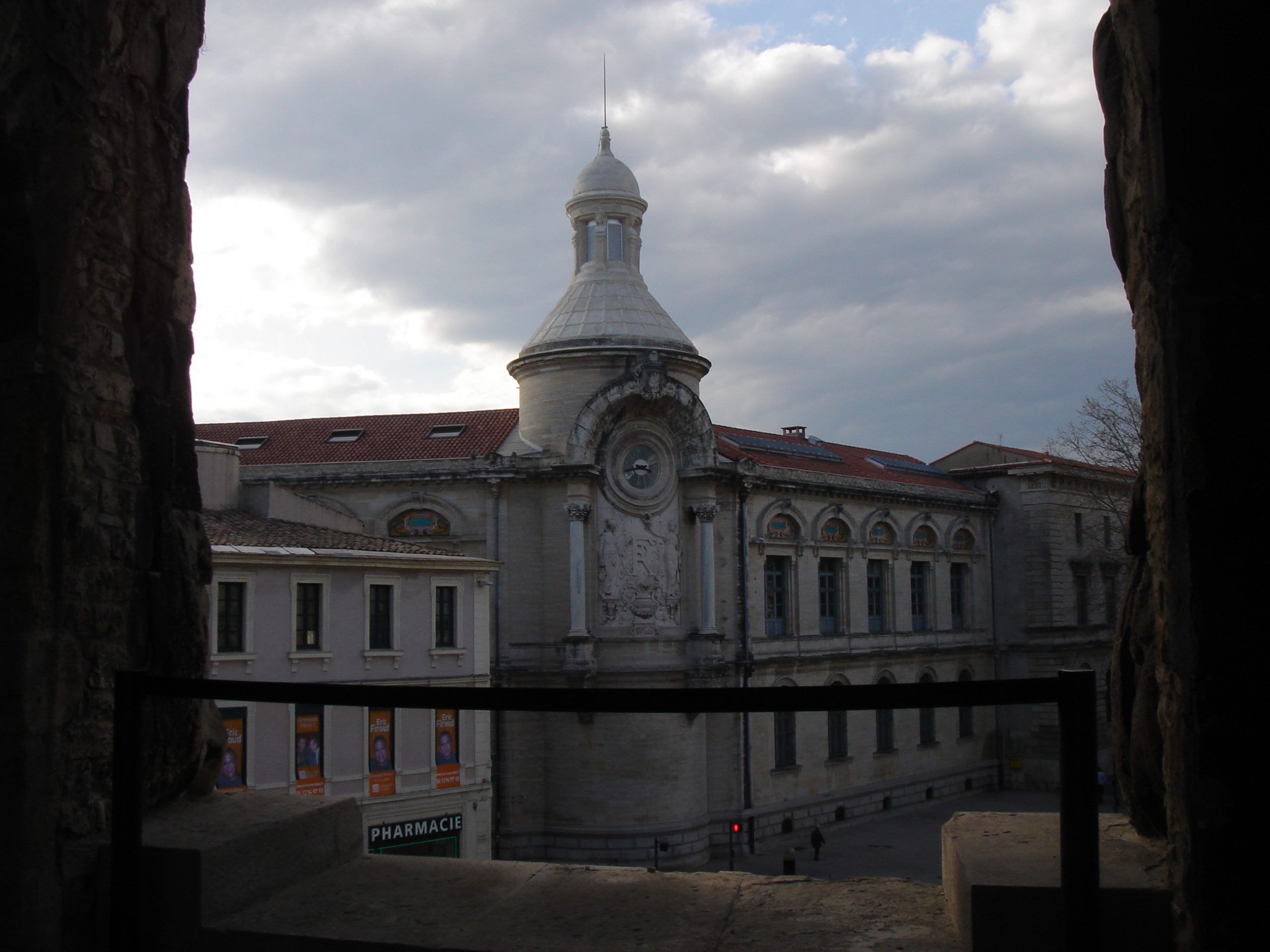 View from within the Roman amphitheatre in Nîmes, looking out toward a domed civic building with ornate stonework and a clock.