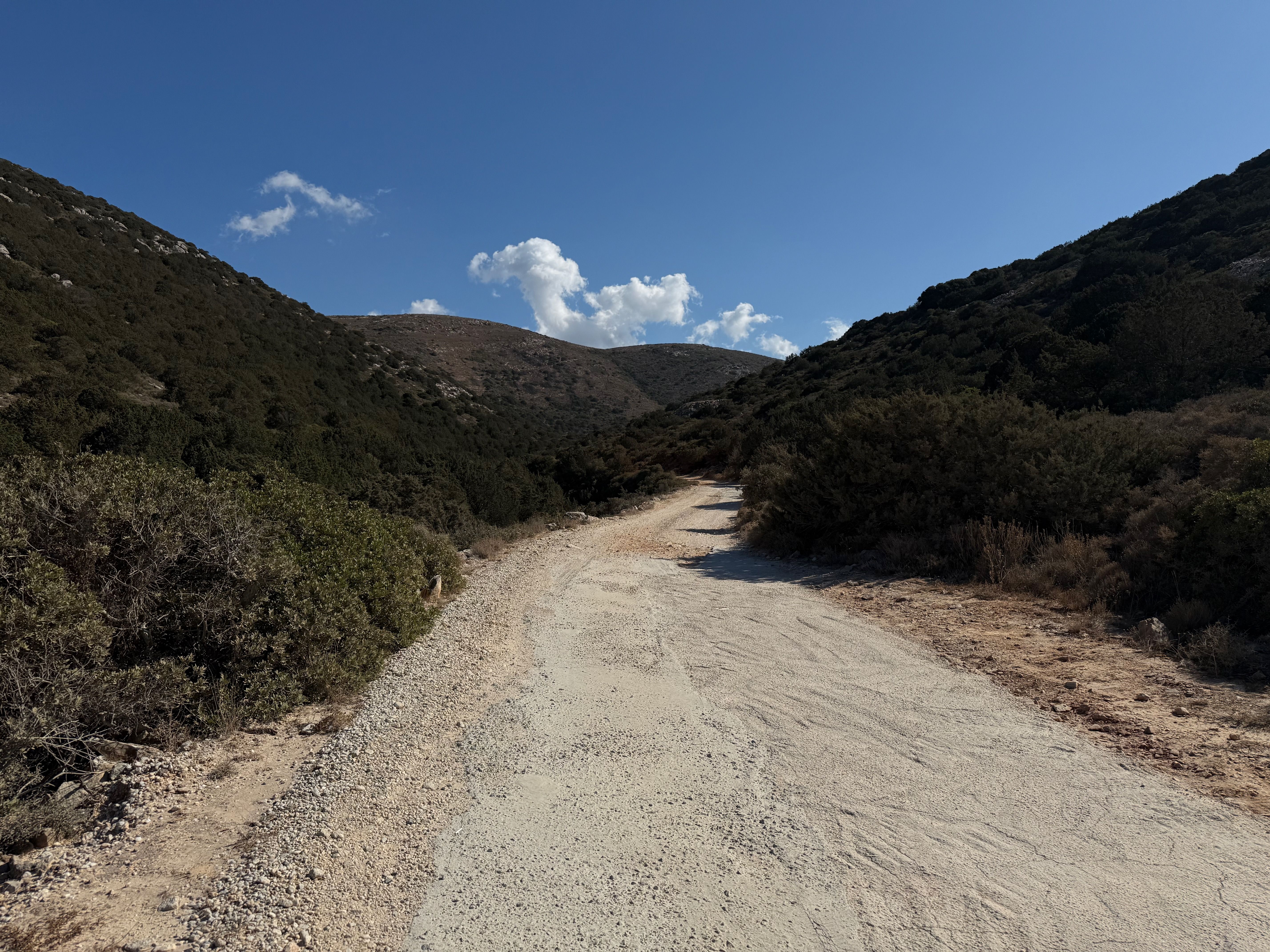 A dirt road whose surface consists of crushed marble leads into the distance, surrounded by wooded hills.