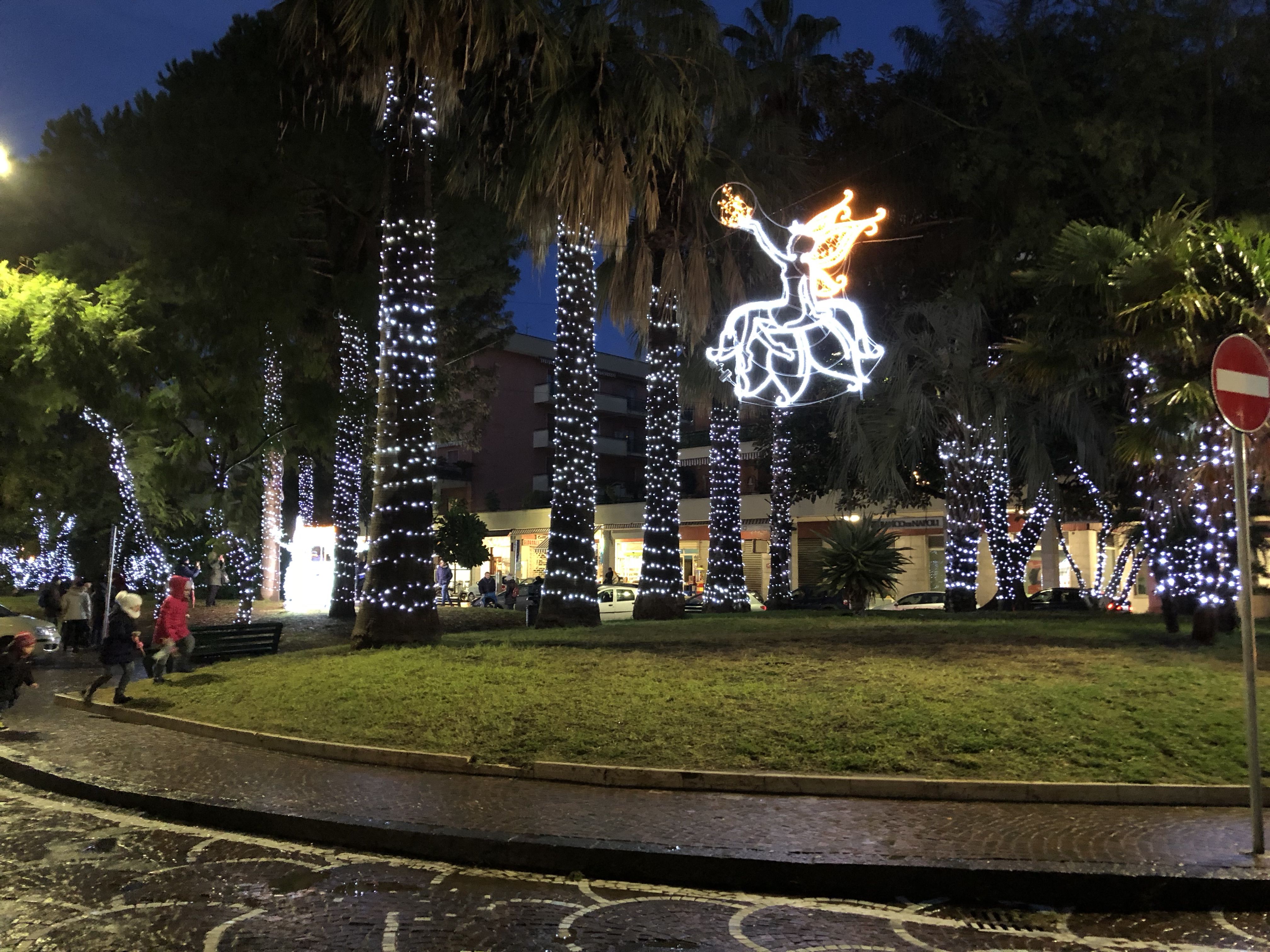 A grassed area in the middle of a square in Sorrento. All the  trees are festooned in Christmas lights.