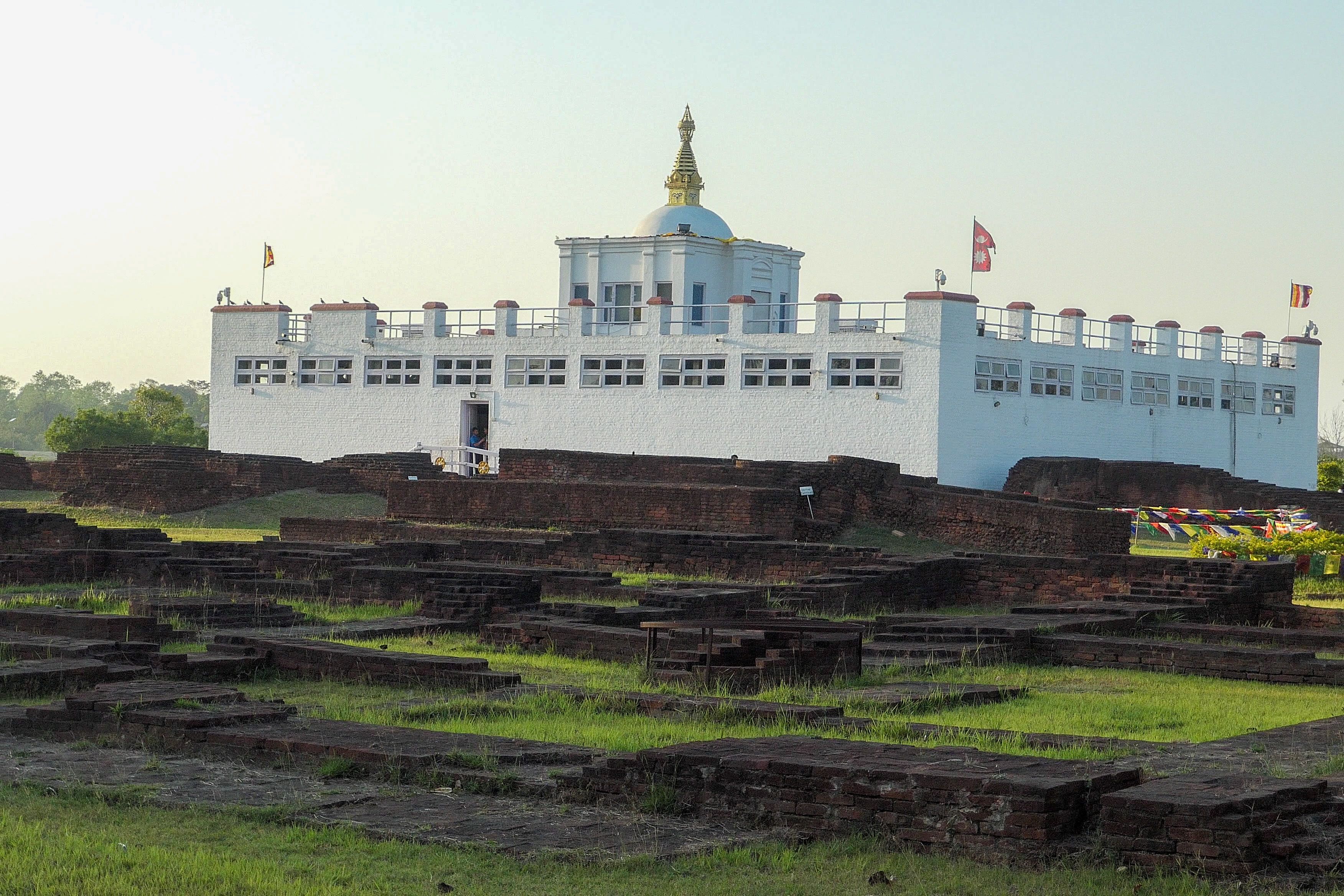 The Maya Devi Temple in Lumbinī, a white building with a golden spire, surrounded by ruins of ancient brick foundations.