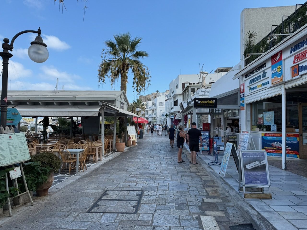 Looking along the road that runs along the edge of the bay in Naxos. On the left, the covered seating areas of tavernas, on the right, the tavernas themselves.