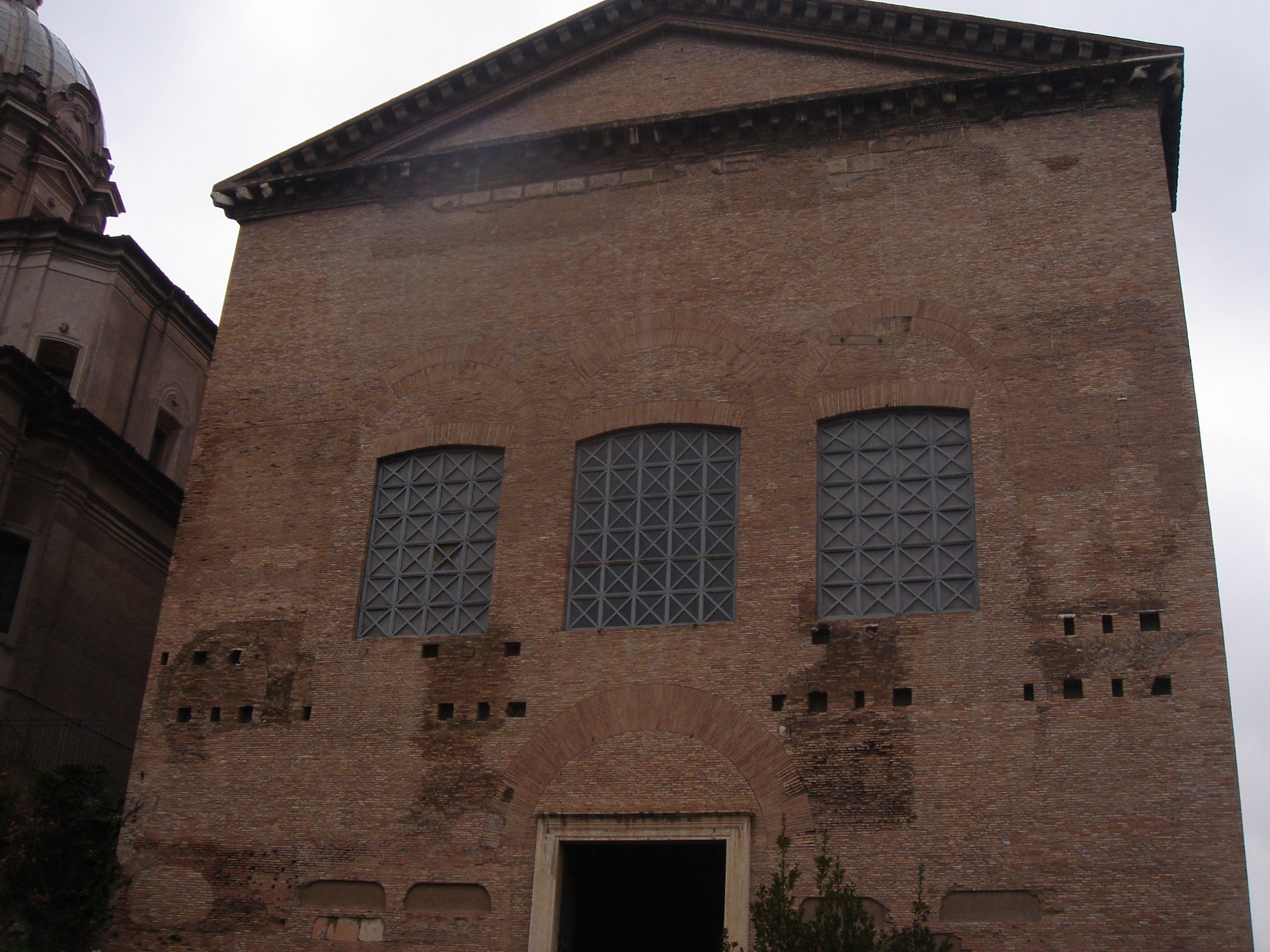 Exterior of the Curia Julia in the Roman Forum, showing a plain brick façade with three high windows and a simple central entrance.