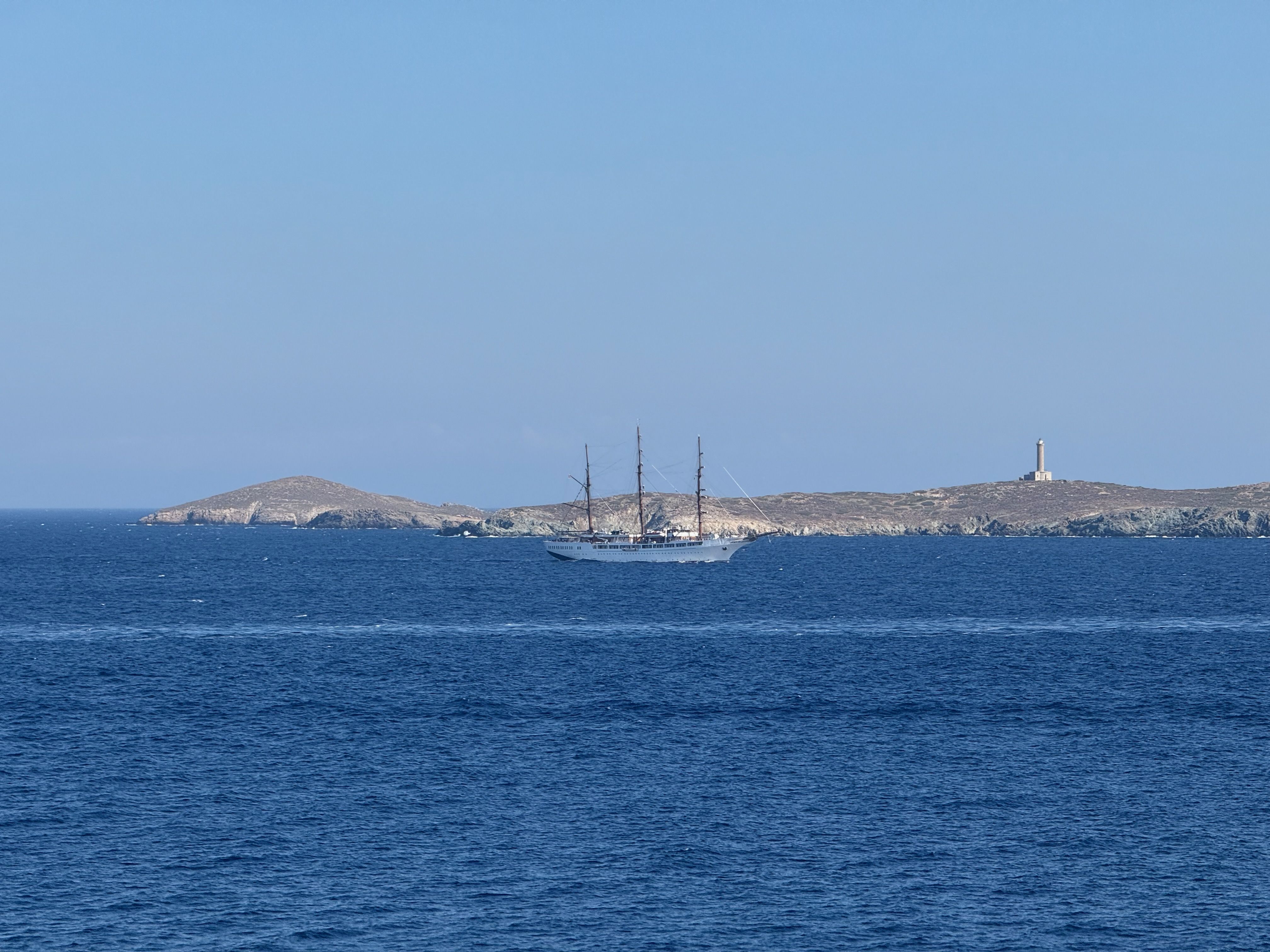 A distant three-masted boat sails through Syros harbour.