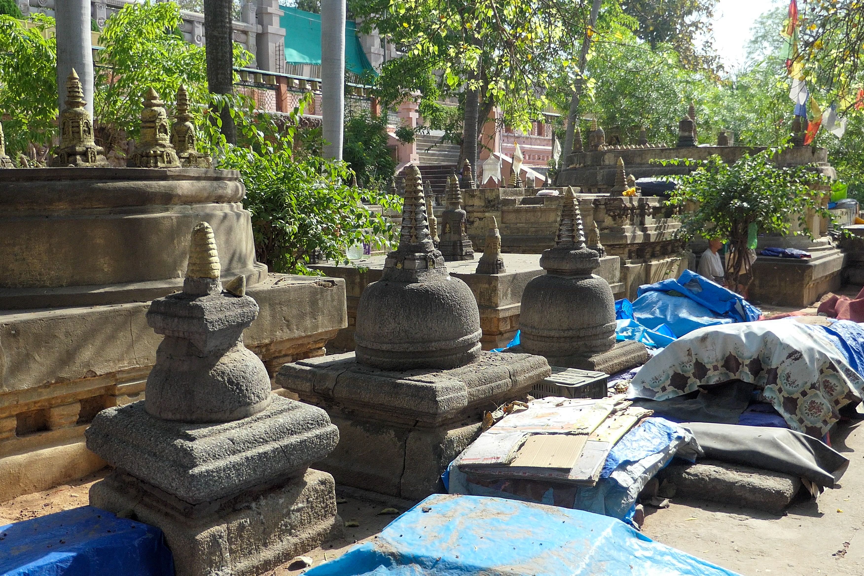 Stone stupas and miniature shrines among greenery and tarps within the Mahabodhi Temple complex in Bodhgaya.