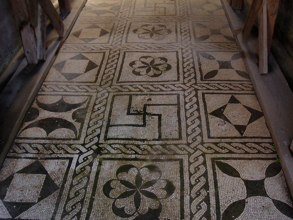 Intricate black-and-white mosaic floor in Herculaneum, featuring floral and geometric patterns set within square panels.