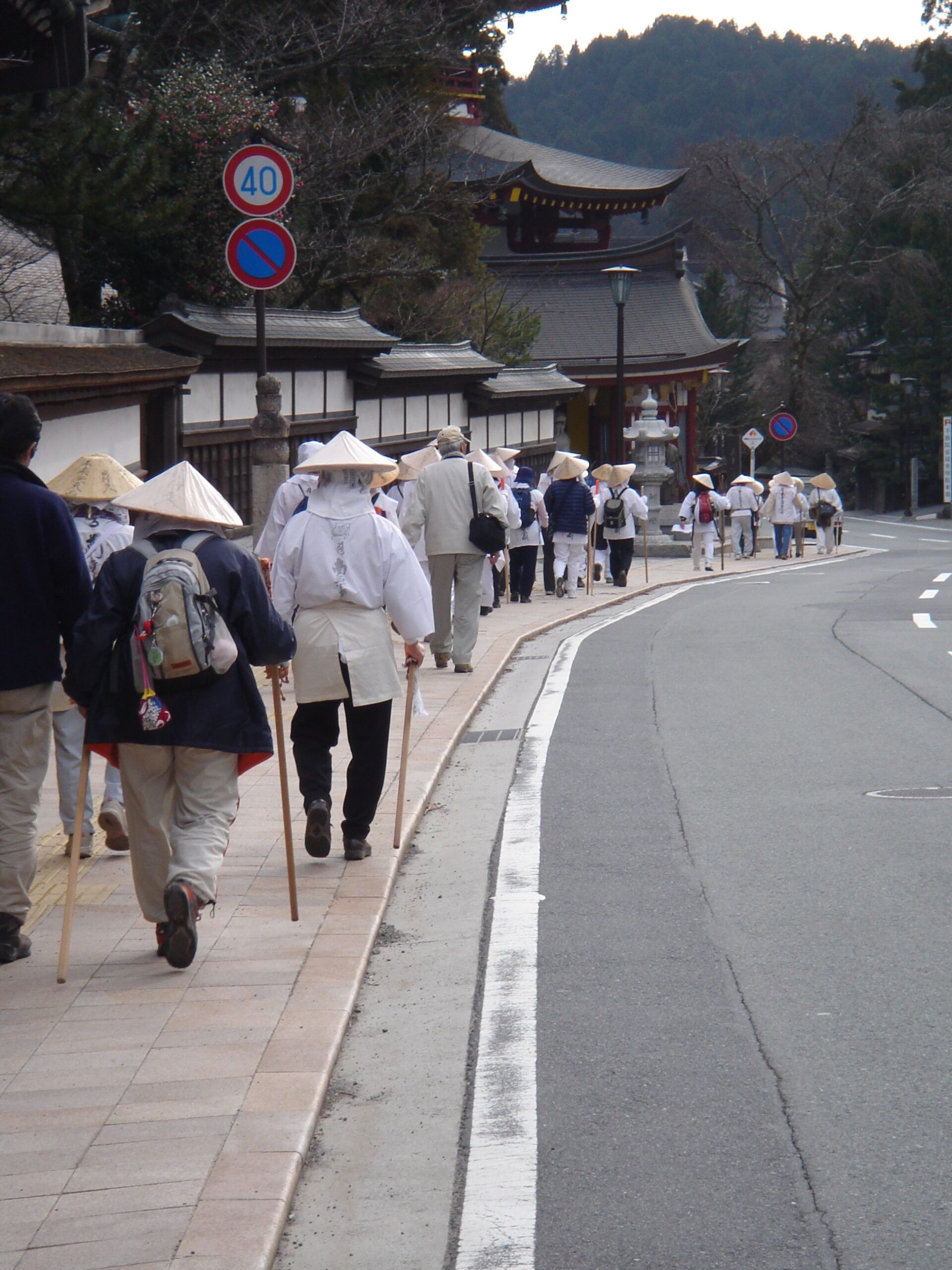 Pilgrims in traditional dress walking along a road near temple buildings in Japan.
