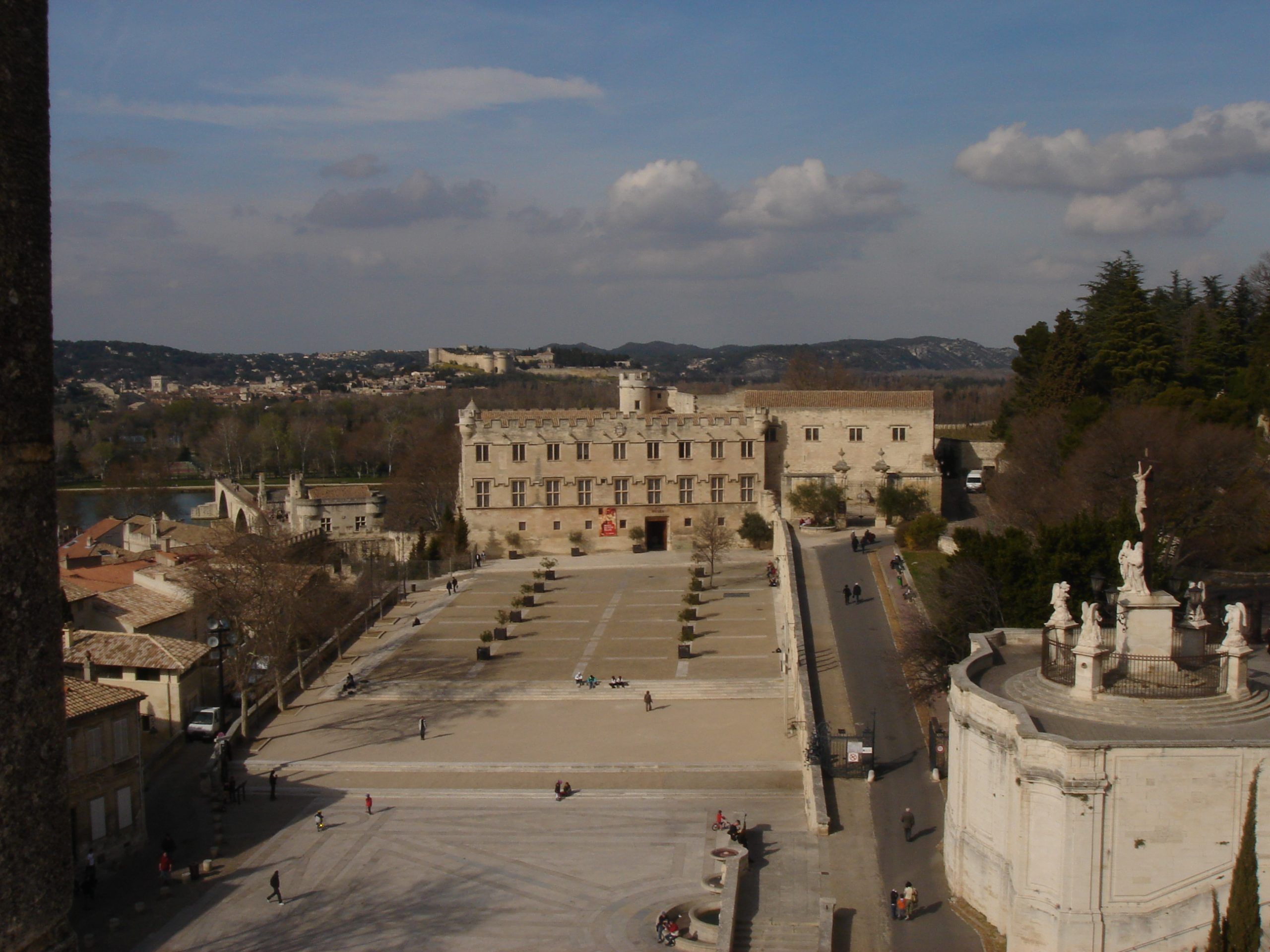 Panoramic view of a square in Avignon from above, with the Rhône River and distant hills in the background.
