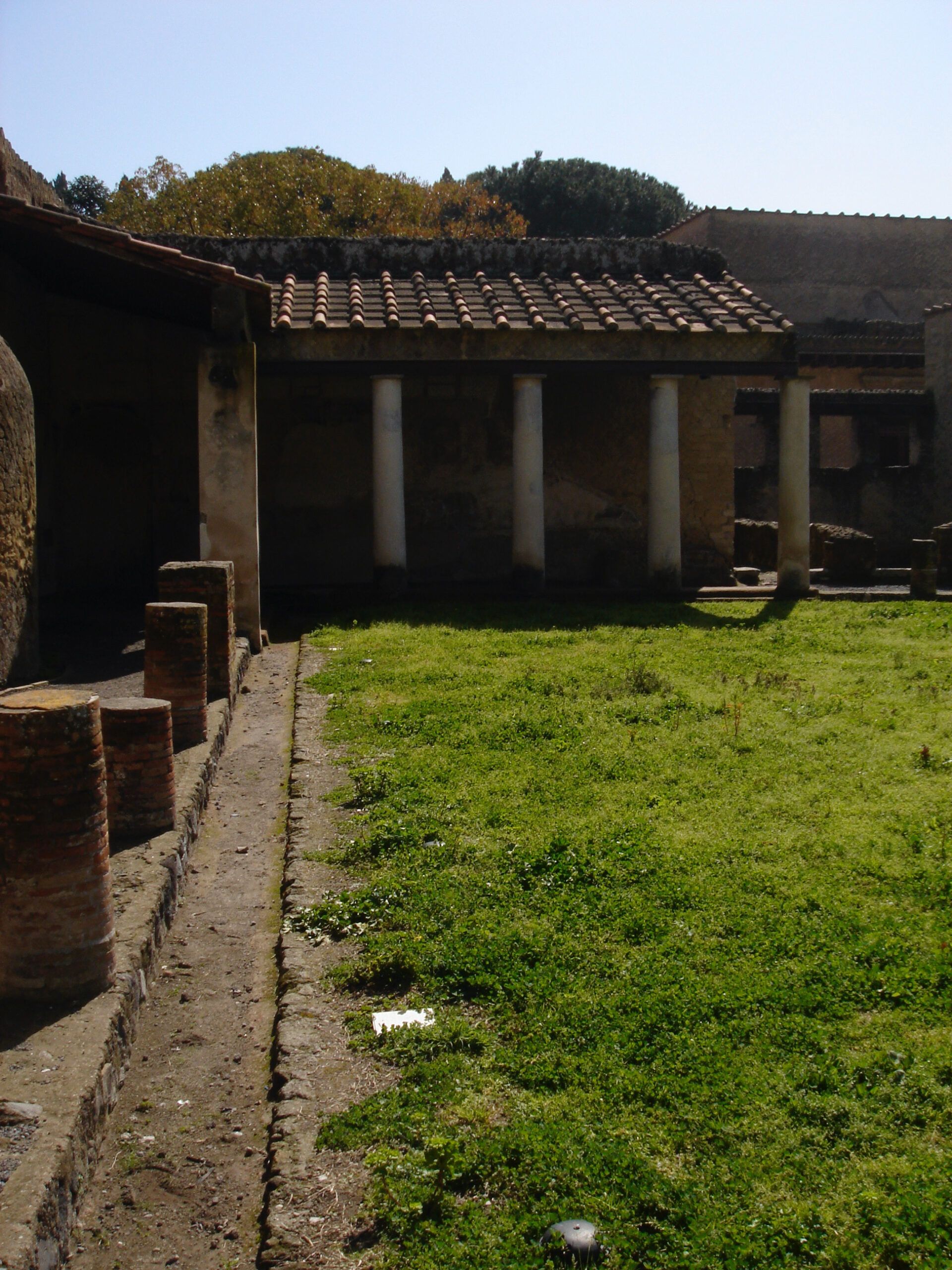 Peristyle garden in a Roman house at Herculaneum, bordered by white columns and low brick walls, with a grassy courtyard in the center.