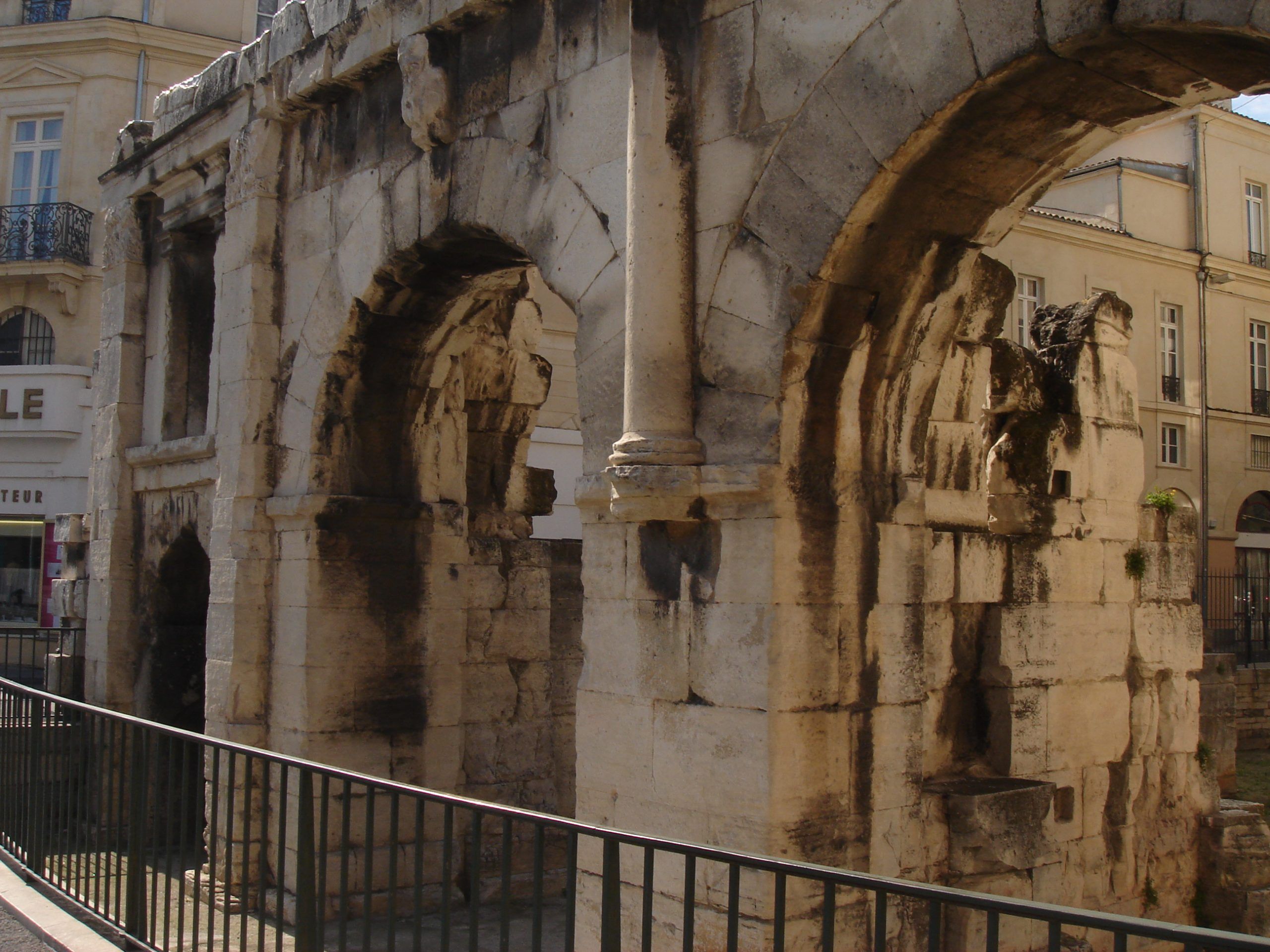 Side view of an ancient Roman gateway in Nîmes with multiple arches and weathered stone.