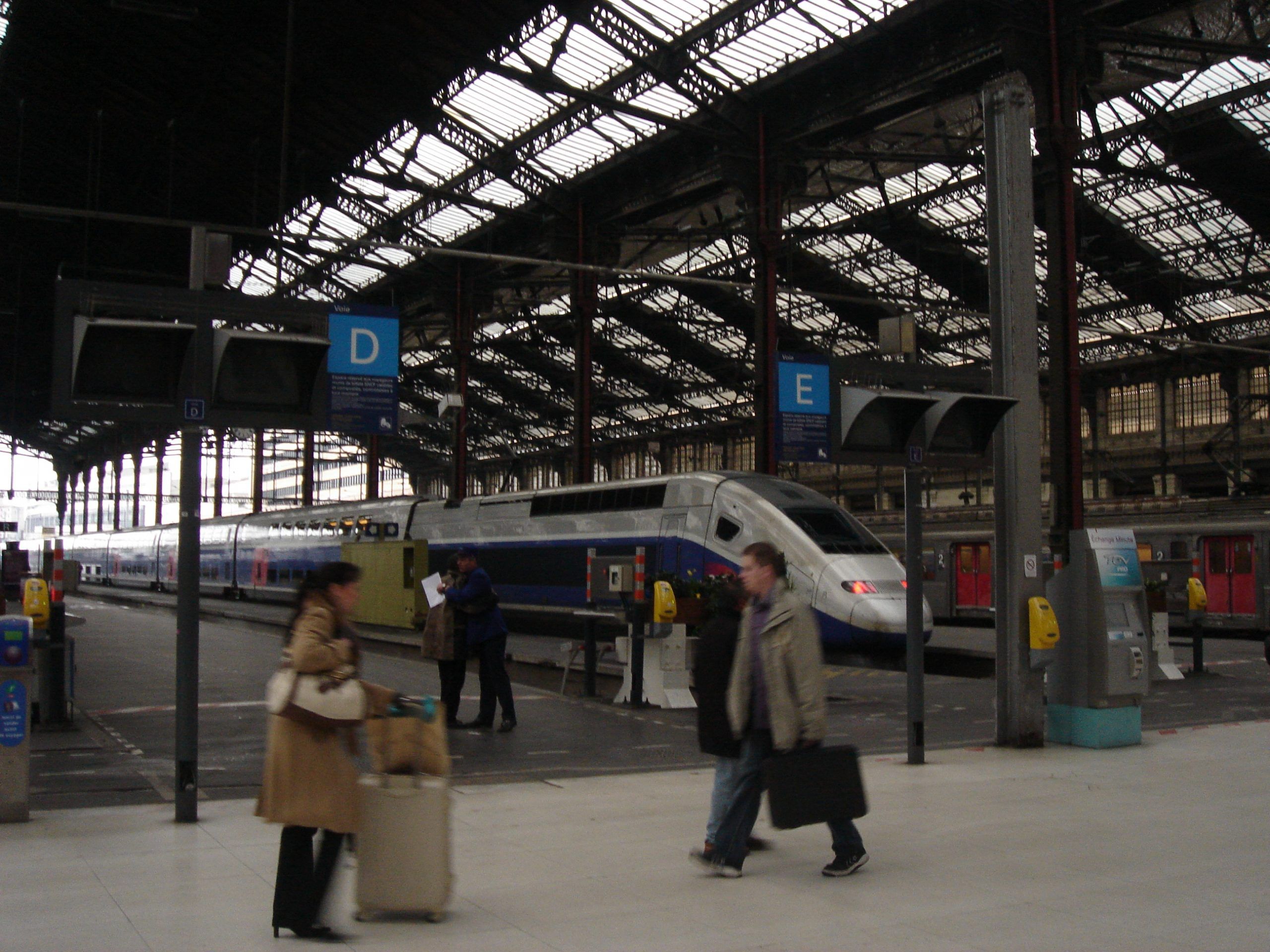 TGV high-speed train inside a covered station with passengers walking on the platform.