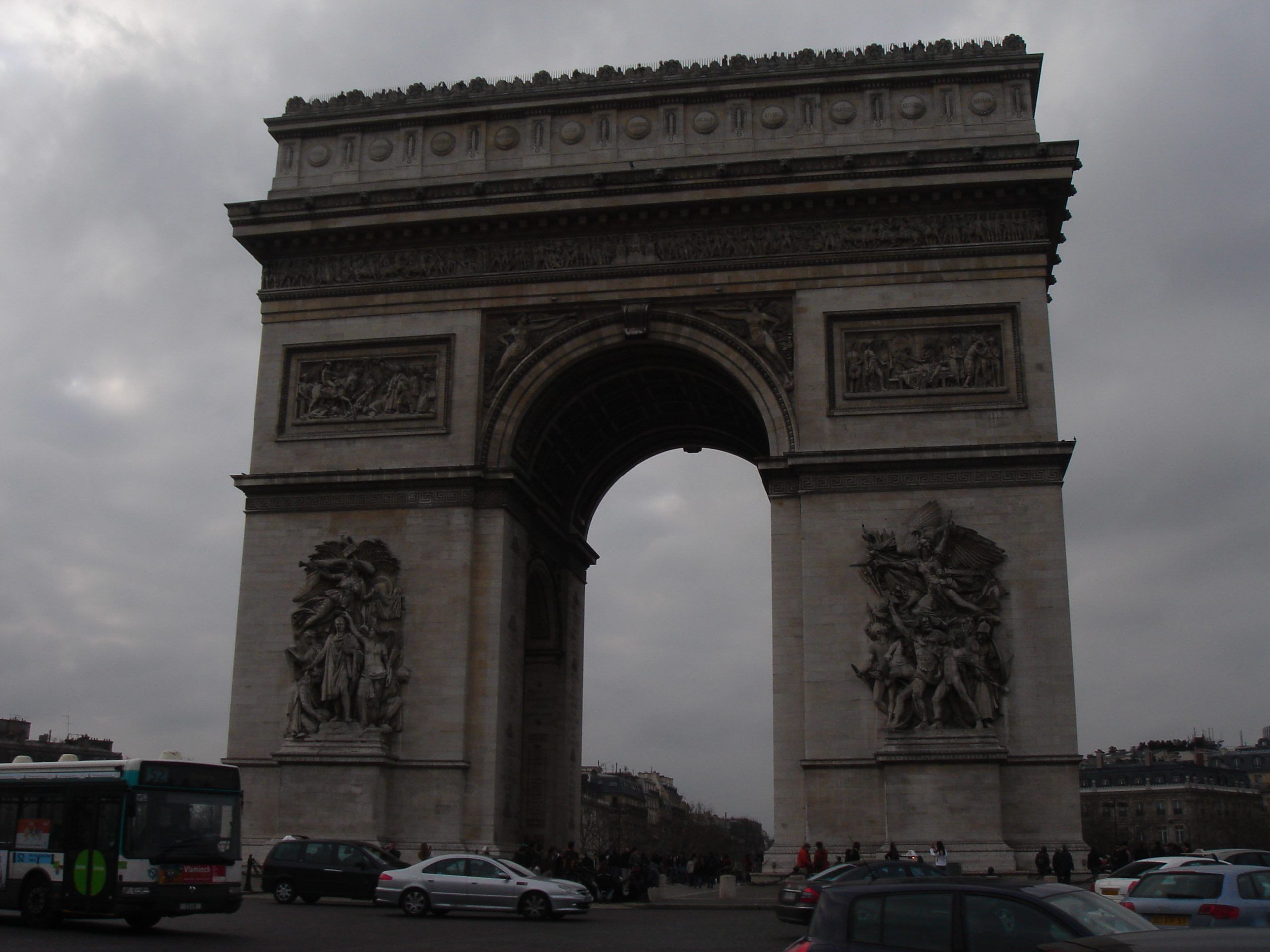 View of the Arc de Triomphe from street level, with traffic and cloudy skies.